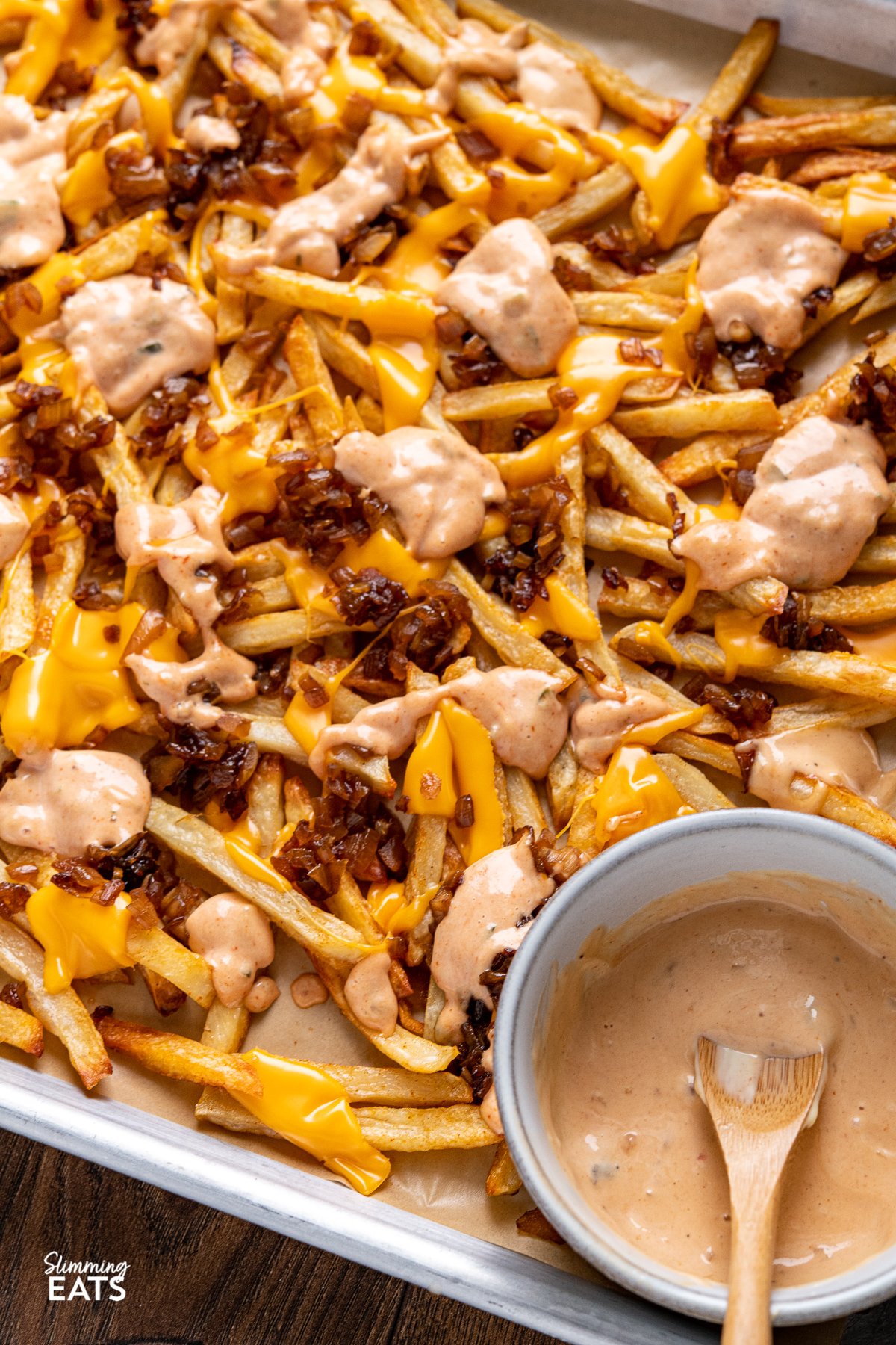 Indulge with these classic fakeaway Animal Style Fries - sweet sauteed onions, golden oven baked fries with melted American cheese and a classic special sauce what more could one want? close up of Copycat Oven Baked Animal Style Fries on a baking tray with a bowl of special sauce