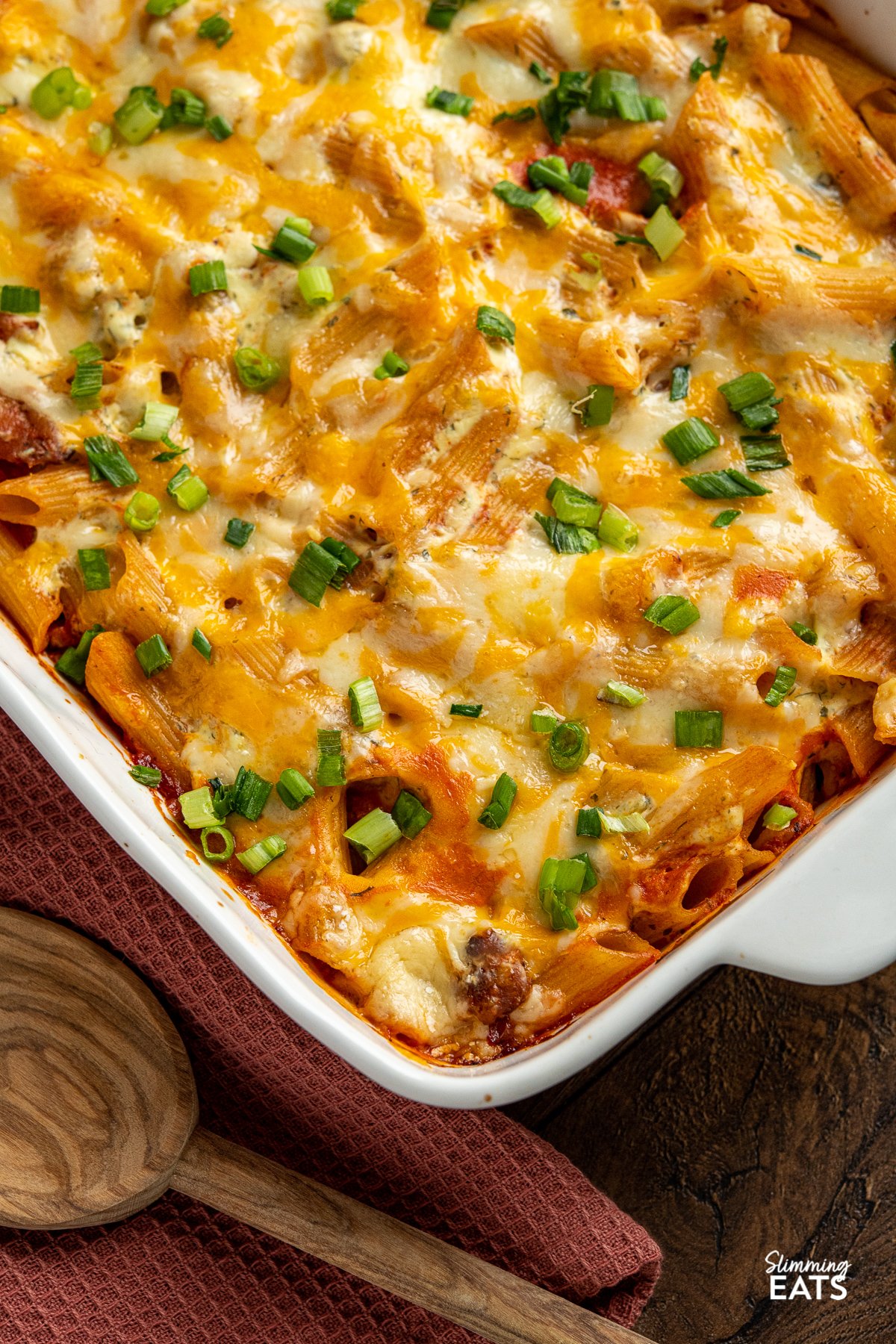 close up of Buffalo Chicken Pasta Bake in white baking dish with olive wooden spoon place in front