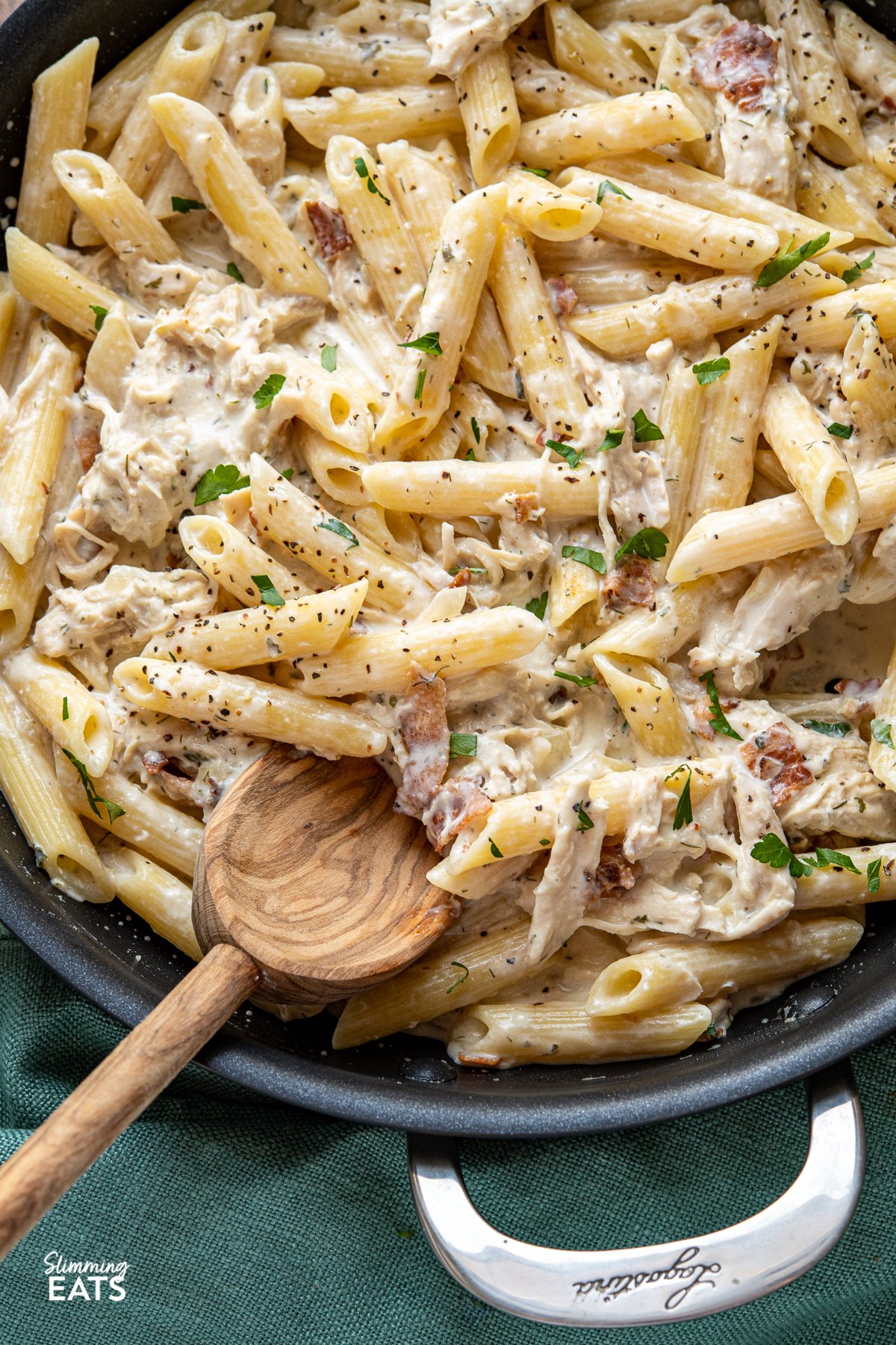 close up of creamy chicken bacon ranch pasta in black frying pan with wooden spoon