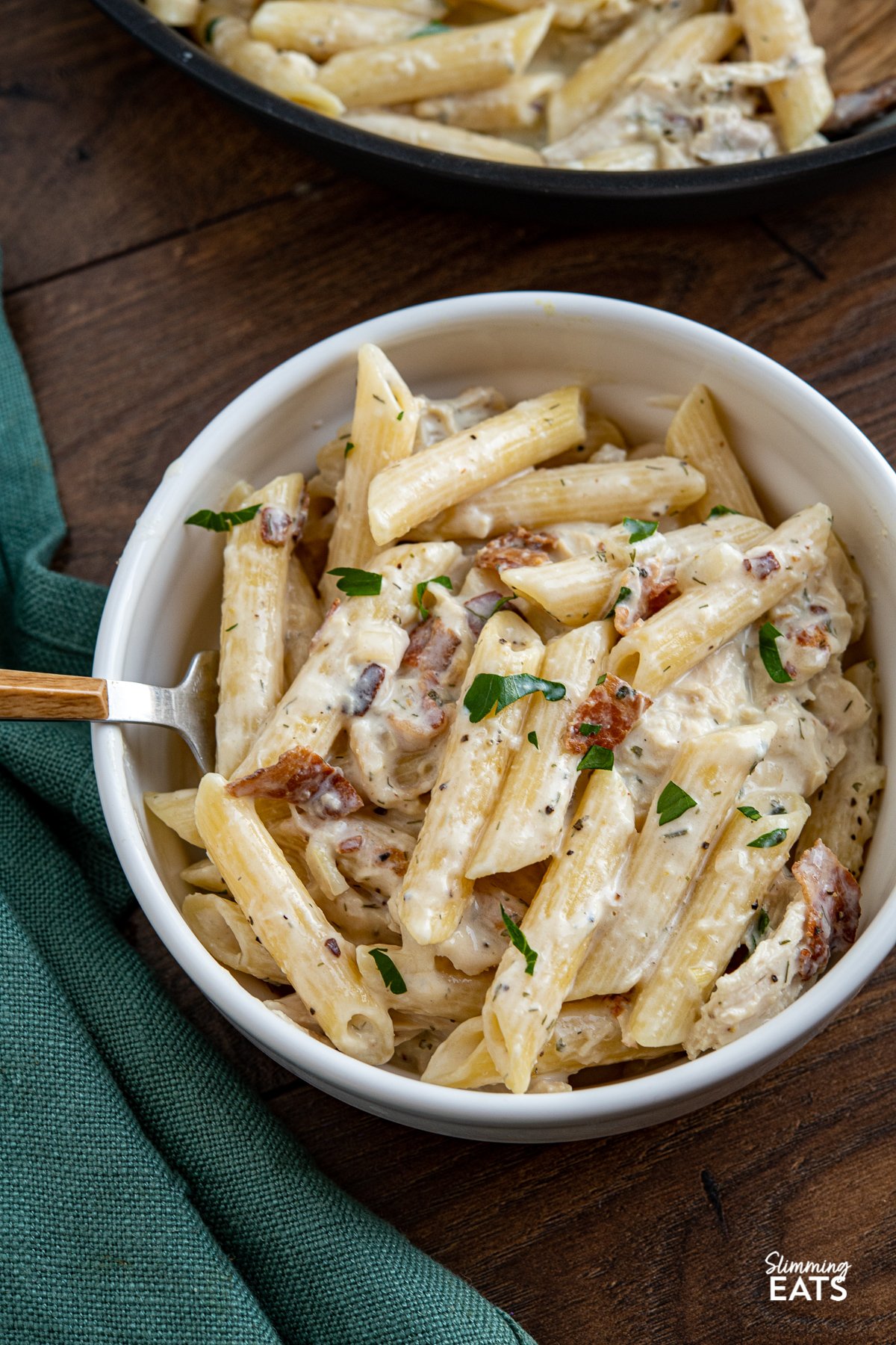 close up of creamy chicken bacon ranch pasta in white bowl with fork