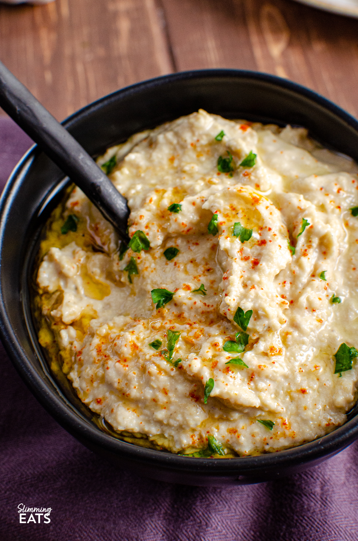 close up of roasted garlic hummus in a black bowl with spooon