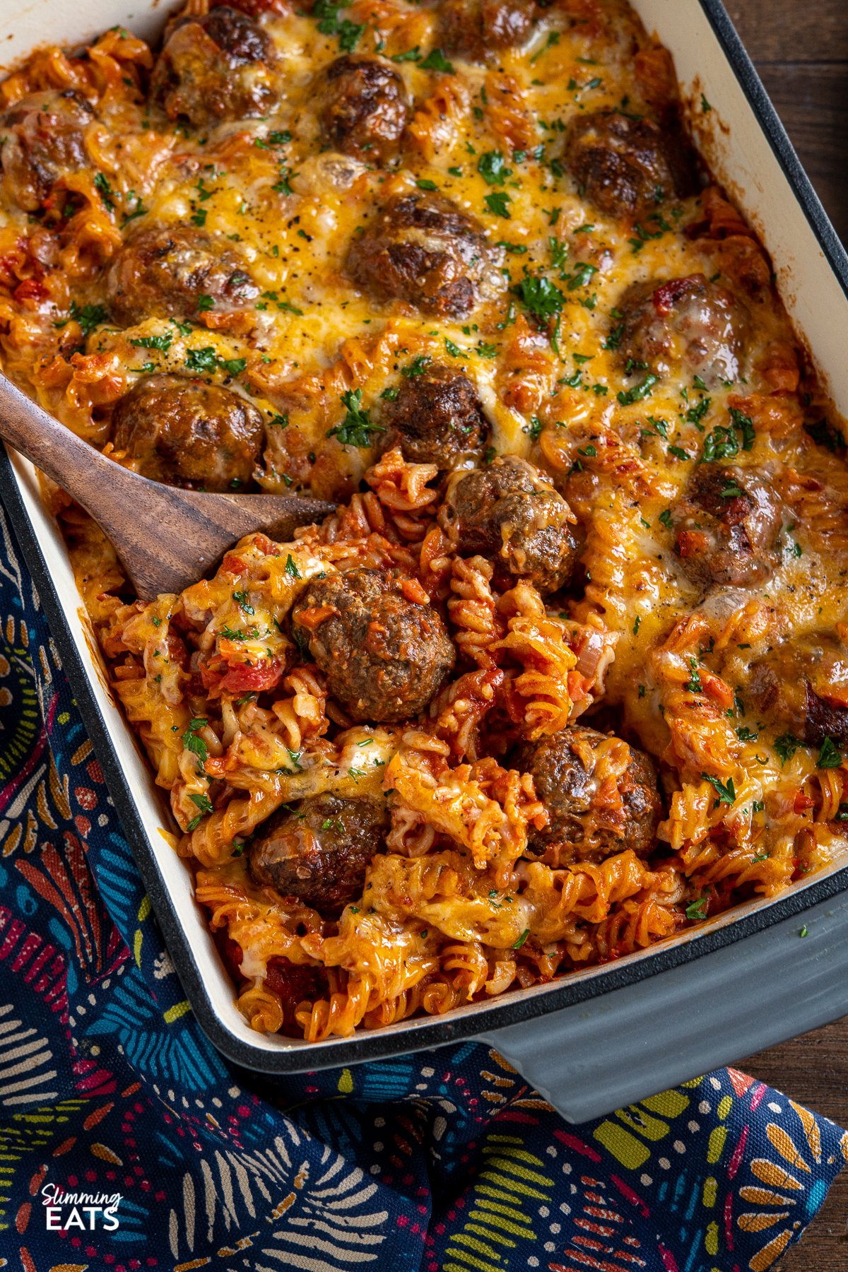 wooden spatula place in dish of cheesy meatball pasta bake