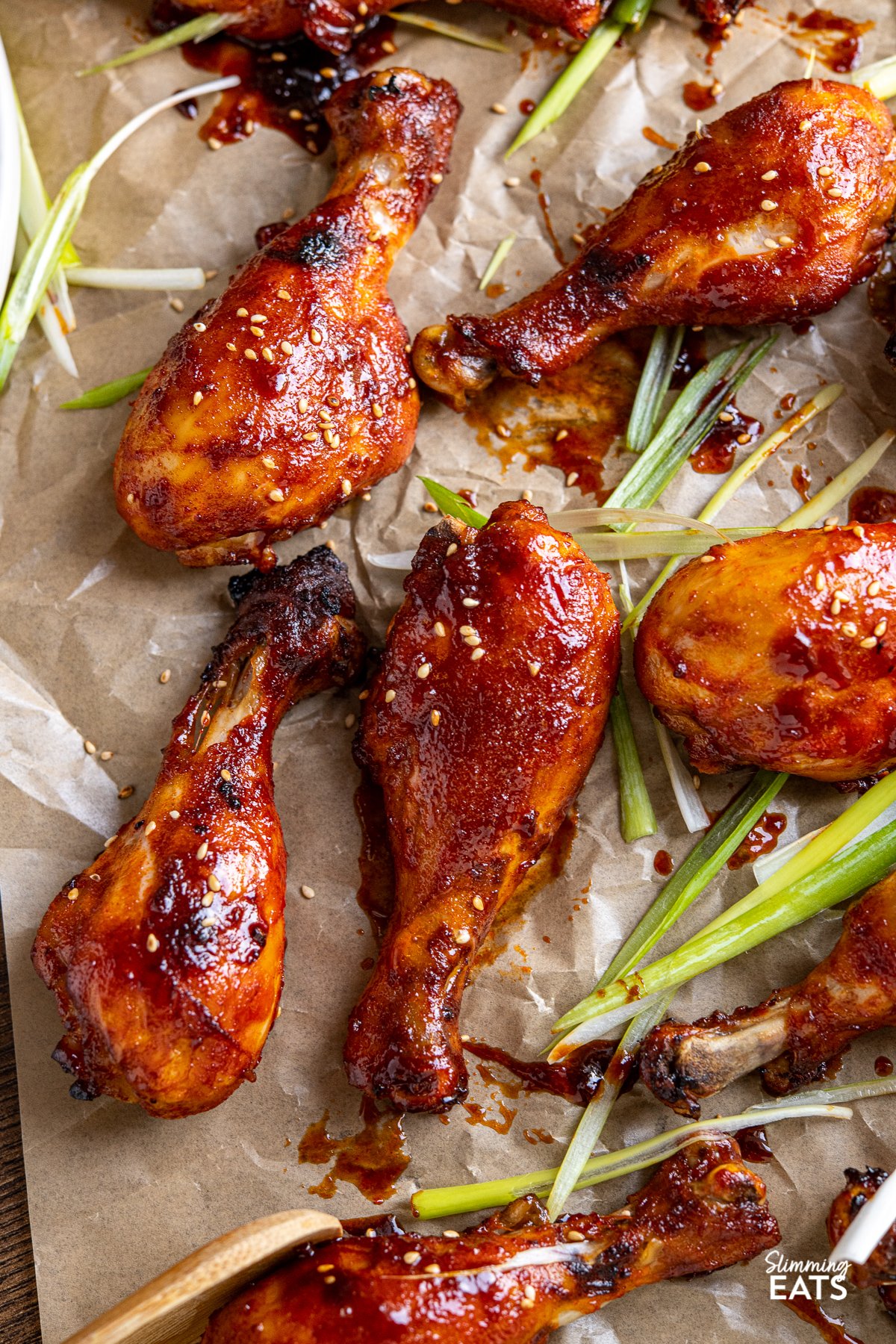 Korean Gochujang Chicken Drumsticks - tender oven baked chicken drumsticks coated in a delicious Korean Gochujang marinade. close up of Korean Gochujang Chicken Drumsticks on a parchment lined baking sheet with scattered slices of green onion