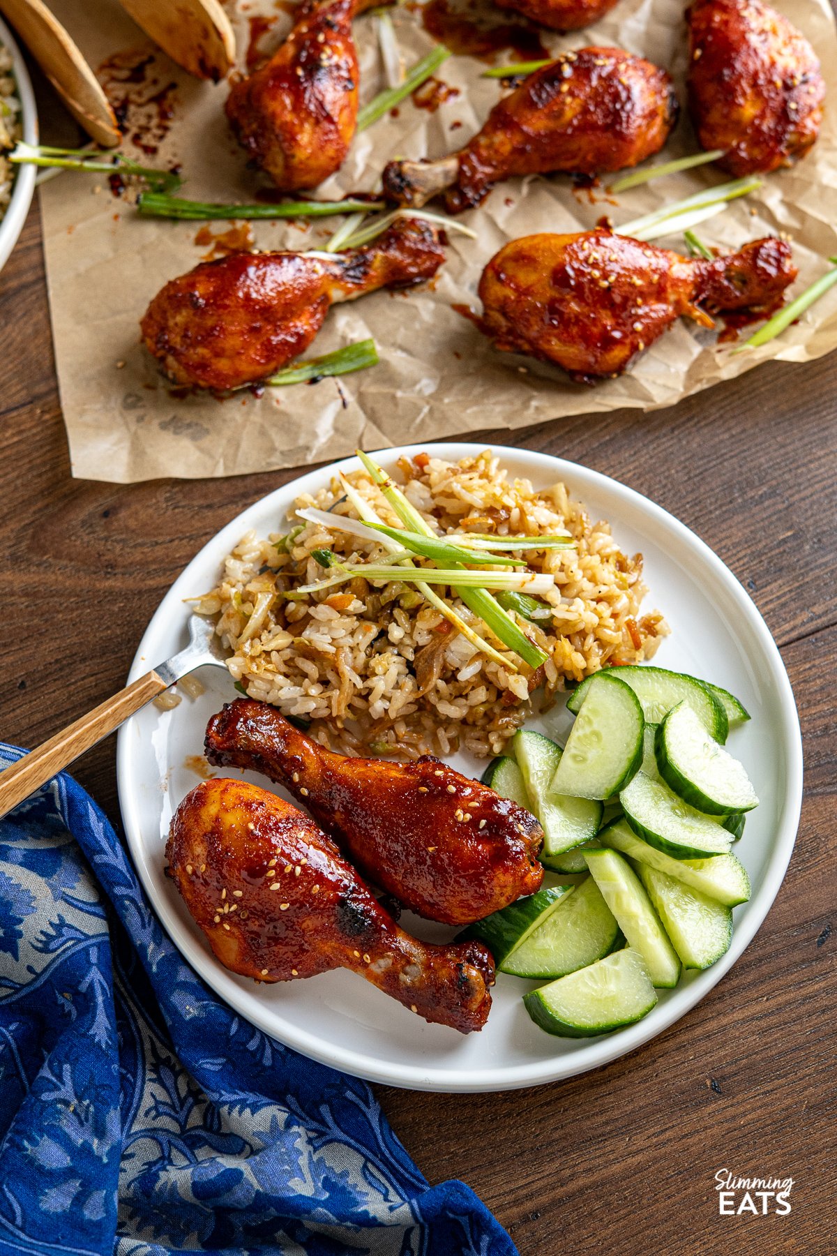 Korean Gochujang Chicken Drumsticks on a white plate with cucumber and fried rice with cabbage. 