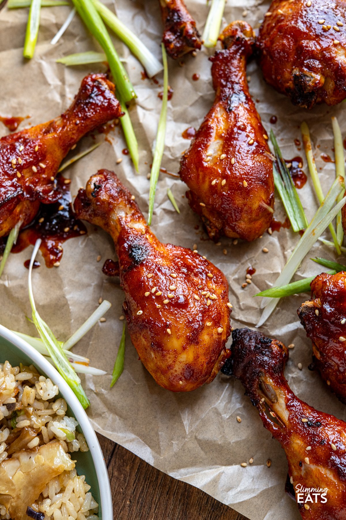 Korean Gochujang Chicken Drumsticks - tender oven baked chicken drumsticks coated in a delicious Korean Gochujang marinade. close up of Korean Gochujang Chicken Drumsticks on a parchment lined baking sheet with scattered slices of green onion