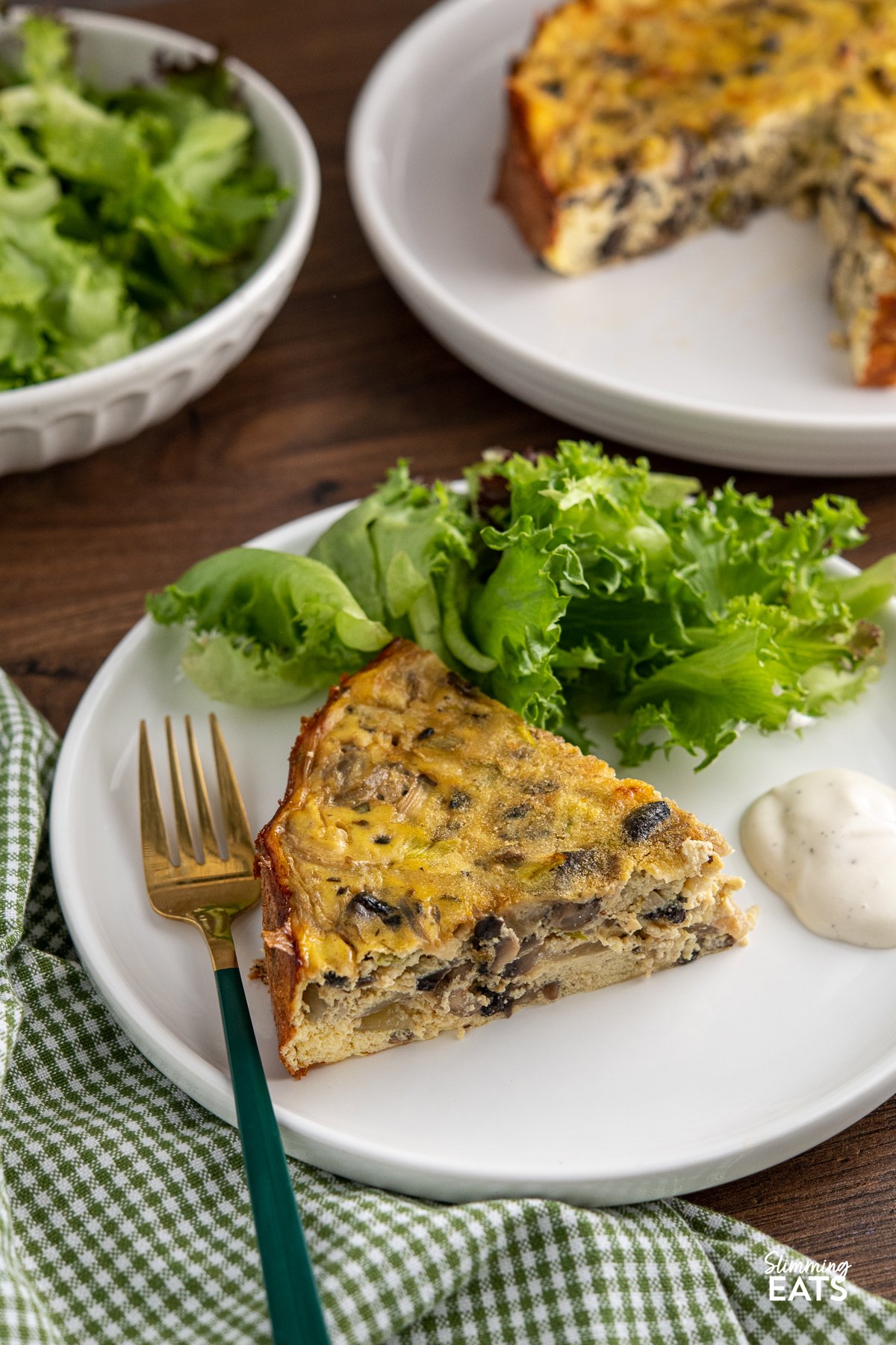 slice of crustless mushroom quiche on white plate with baby greens and ranch