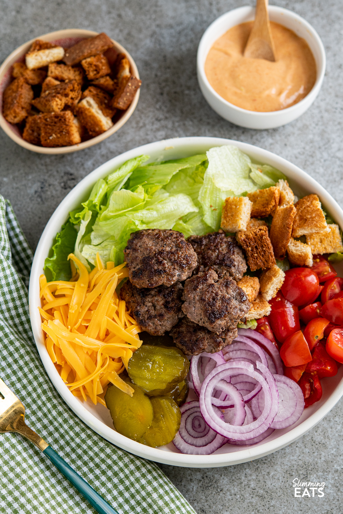 cheeseburger salad in a white bowl with dressing and croutons placed next to bowl