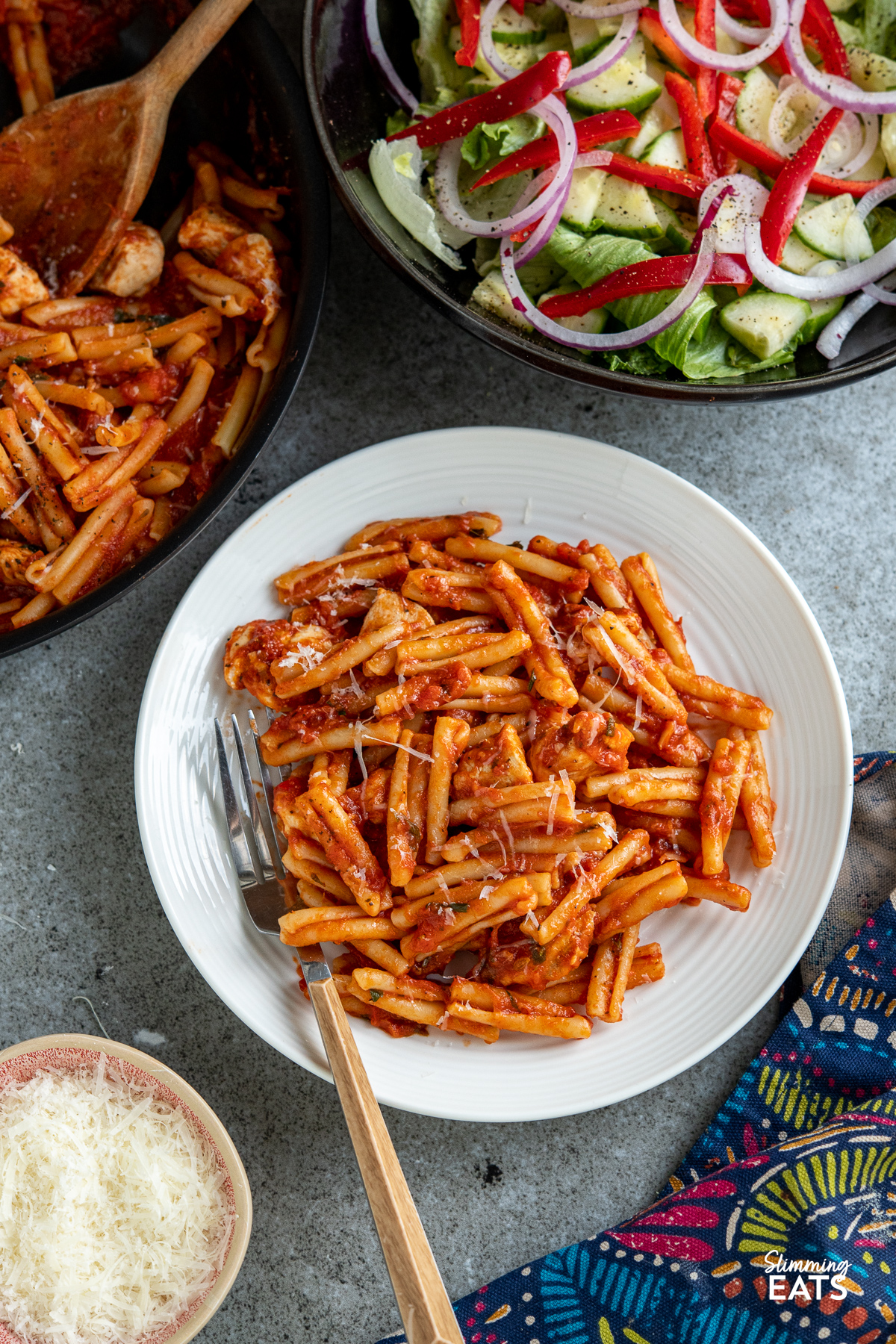 Chicken Arrabbiata Pasta in white plate with bowl of salad and frying pan in background