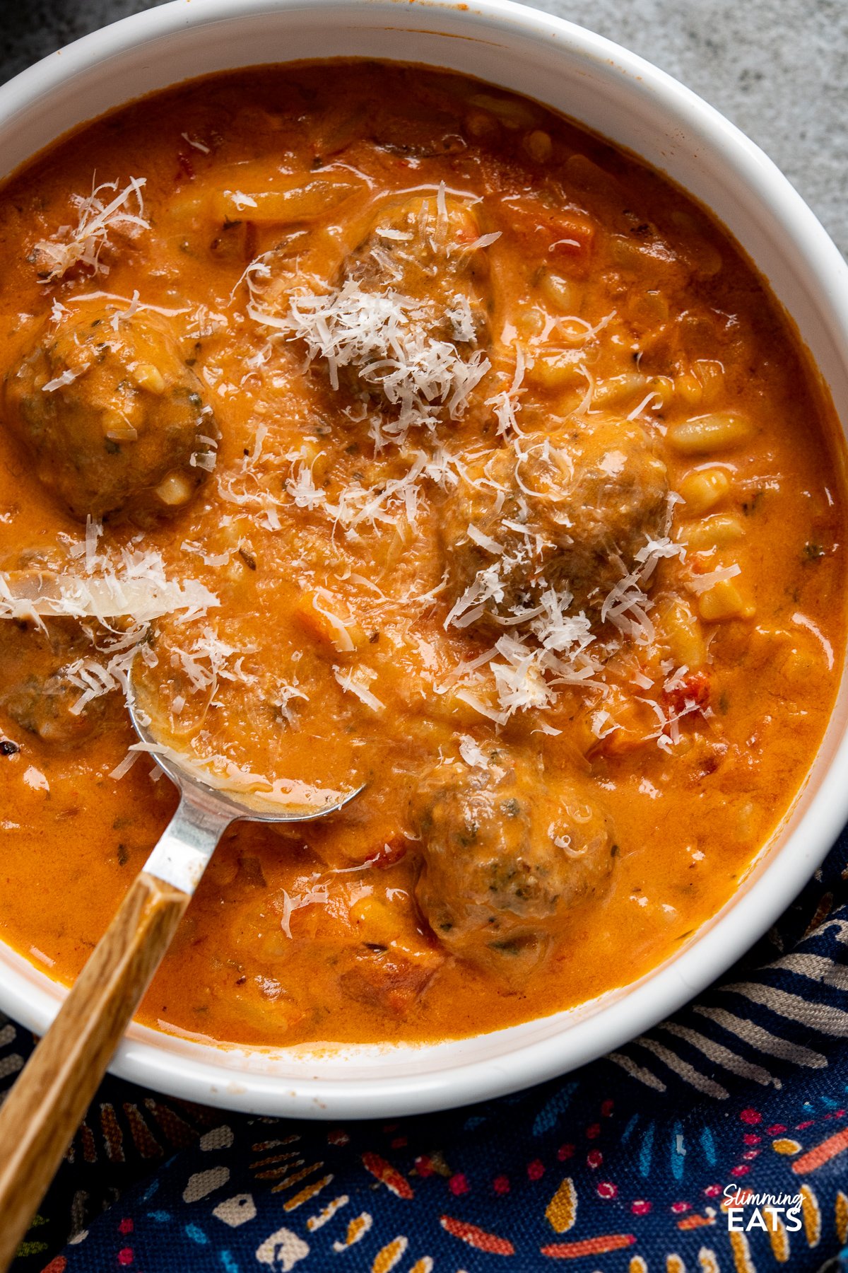 Flavoursome silky creamy tomato soup with orzo pasta and herby garlic chicken meatballs makes this a complete meal in a bowl that the whole family will love. close up of Creamy Tomato Orzo Soup with Chicken Meatballs in a white bowl with spoon and fresh grating of parmesan