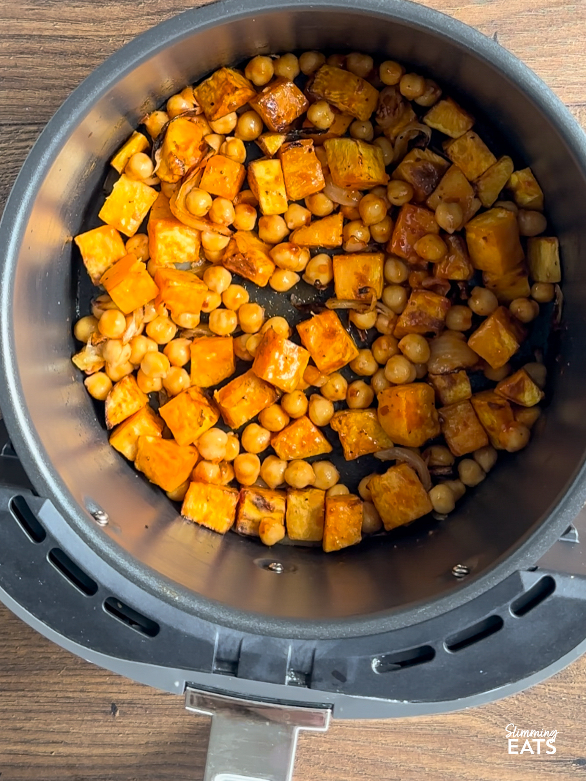 cooked sweet potato and onion in air fryer basket with harissa coated chickpeas