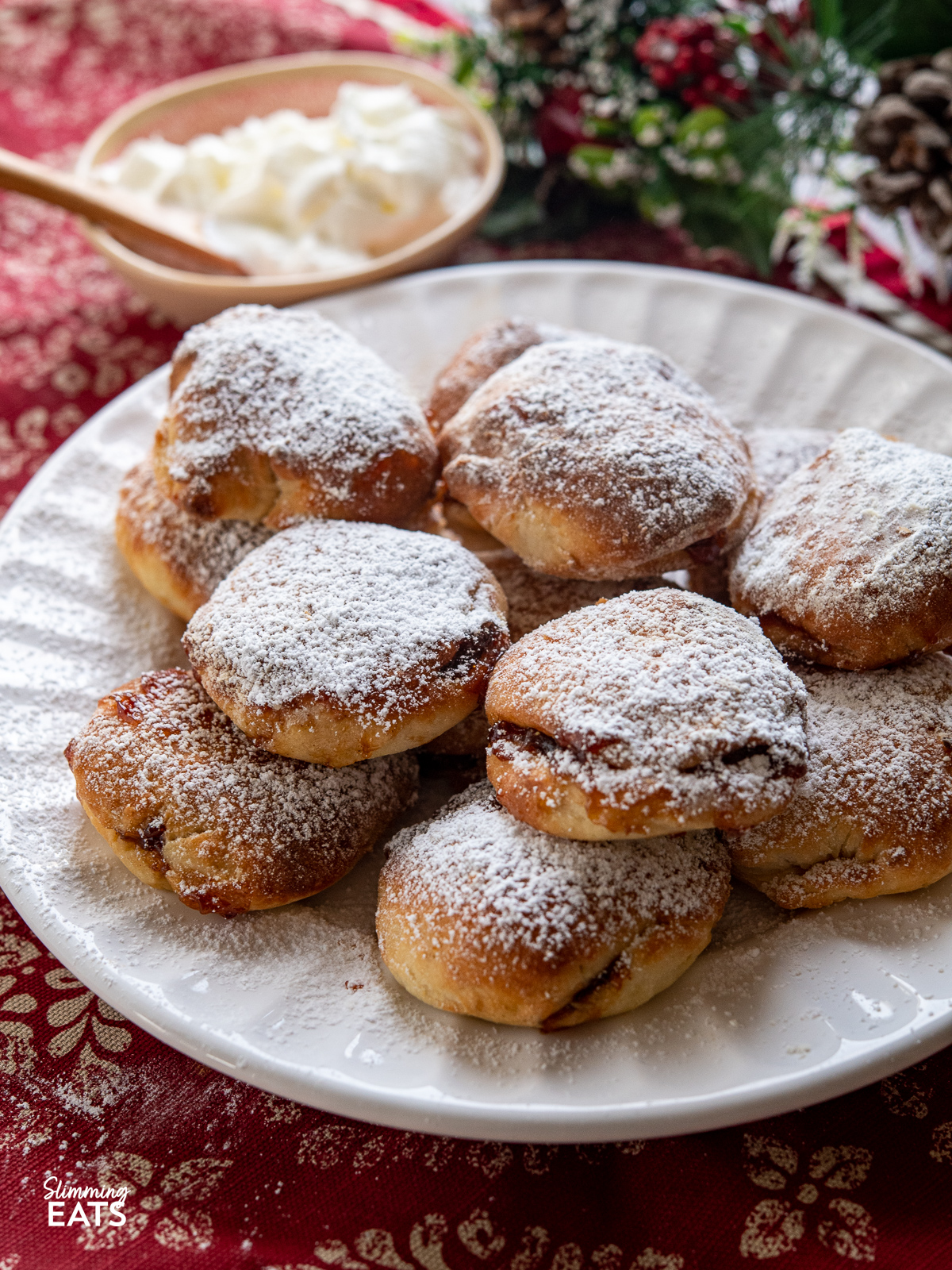 close up of Air Fryer Mince Pie Bites on a white plate dusted with icing sugar with cream behind in a in a bowl 