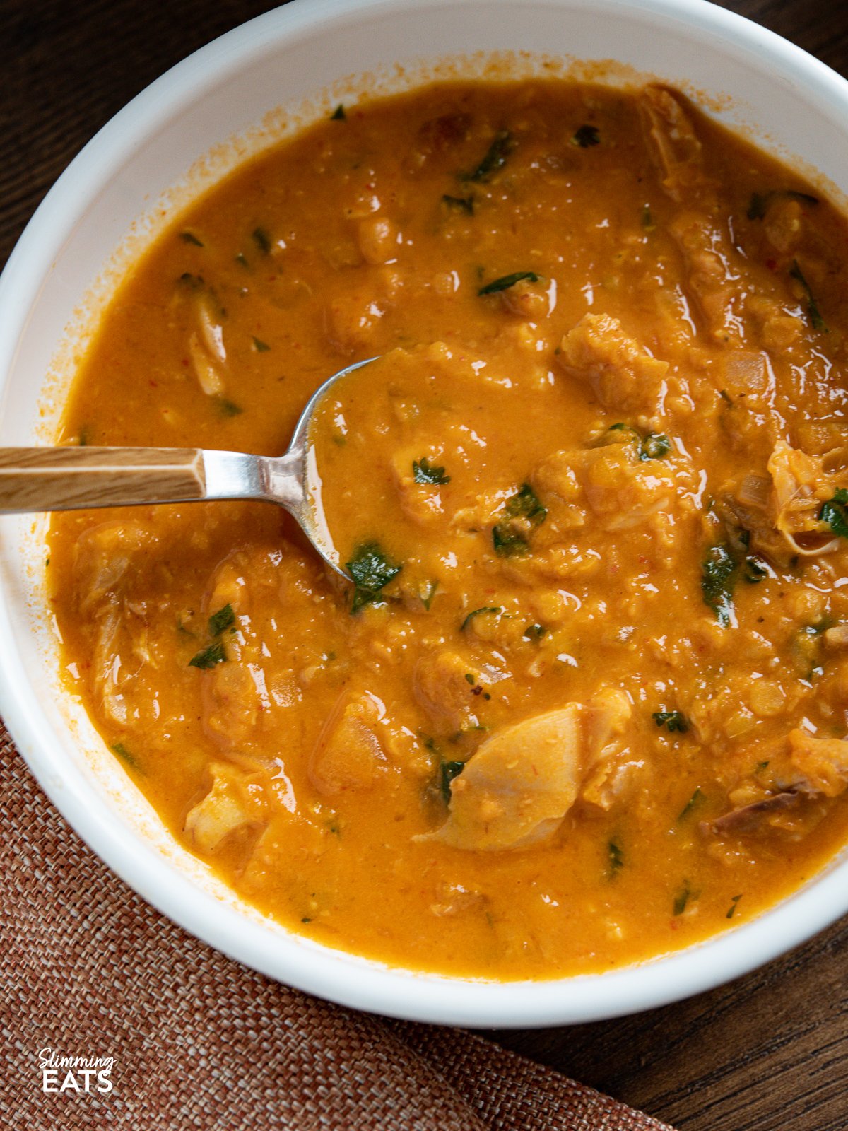 close up of Thai Red Chicken Lentil Soup in a white bowl with spoon