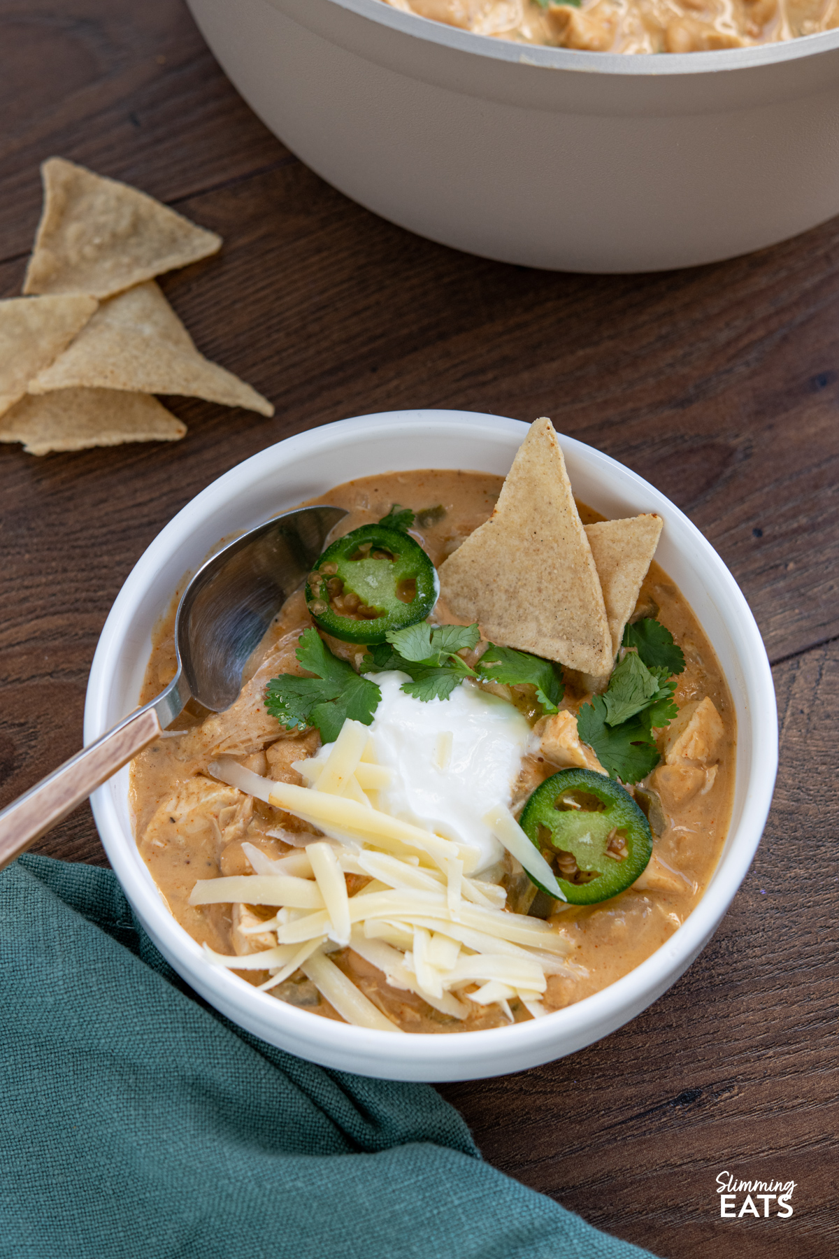 White Chicken Chili in a white bowl with toppings, scattered tortilla chips in background