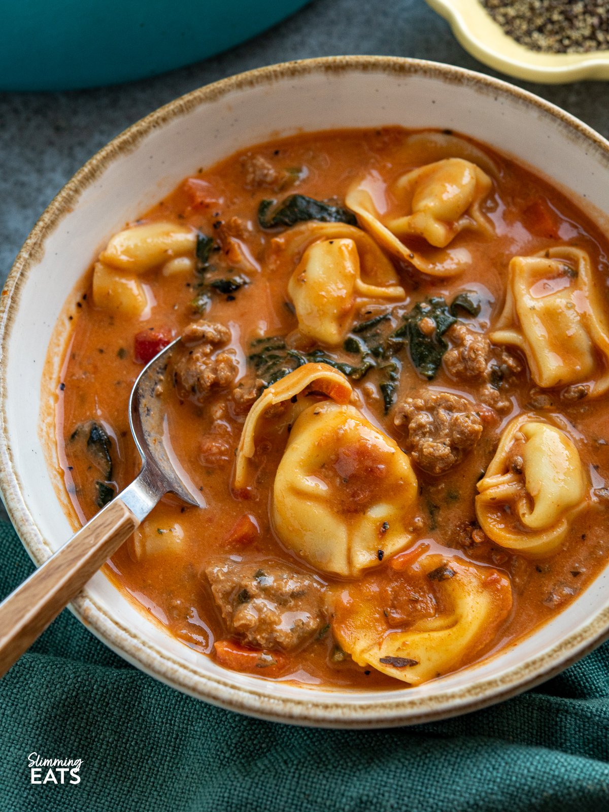 close up of Creamy Italian Sausage Tortellini Soup in a white bowl with light brown rim, spoon placed in bowl