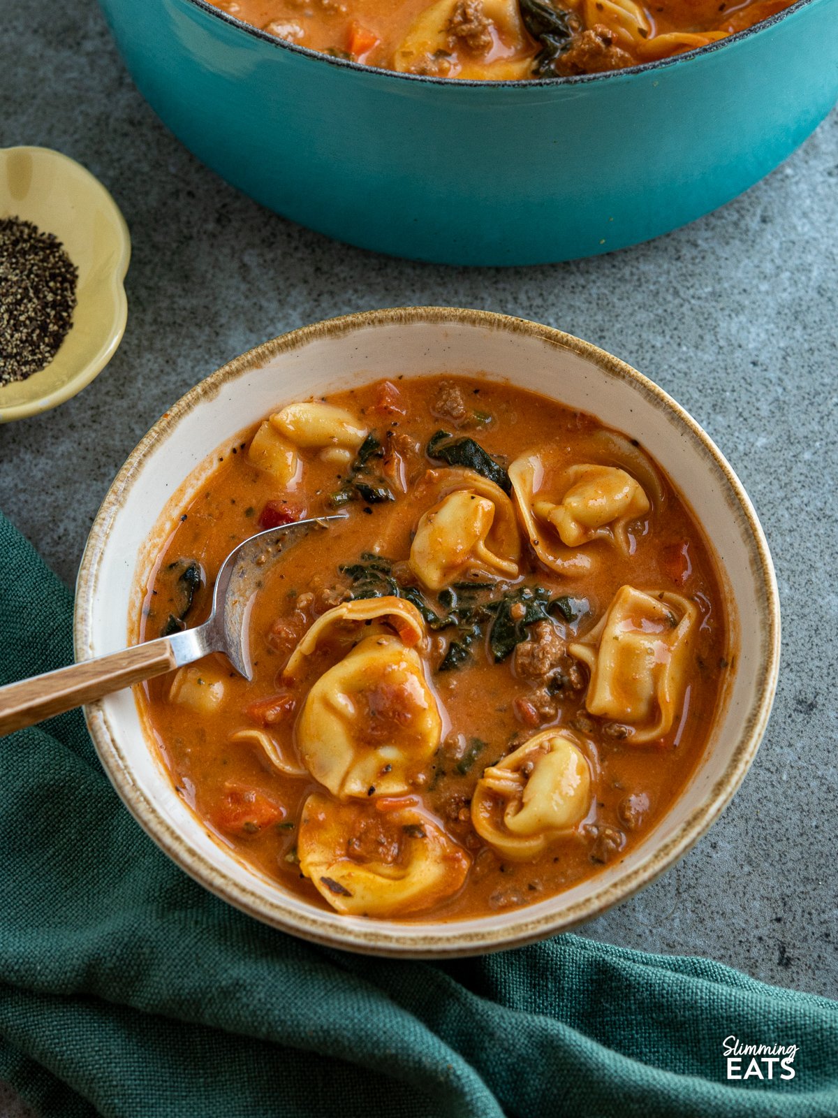 Creamy Italian Sausage Tortellini Soup in a white bowl with light brown rim, spoon placed in bowl