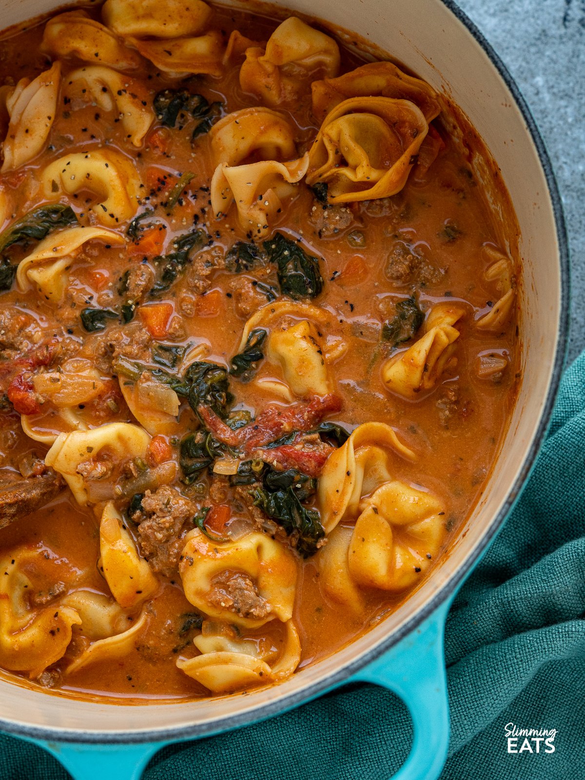 Creamy Tortellini Soup - homemade Italian ground sausage in a delicious light creamy tomato broth with cheese filled tortellini and spinach. close up of Creamy Italian Sausage Tortellini Soup in teal cast iron le creuset
