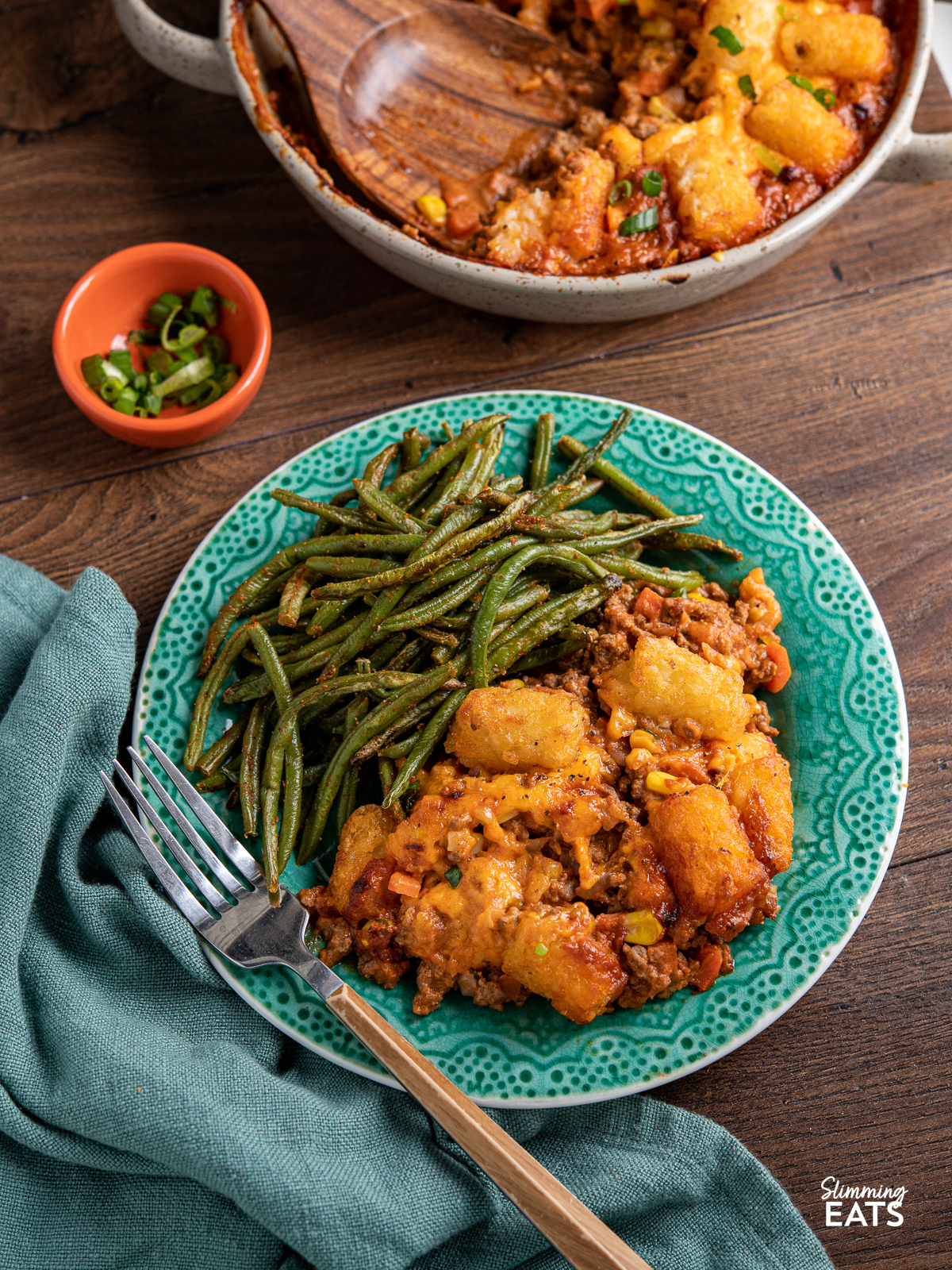 Tater Tot Casserole served up on a turquoise plate with roasted green beans, fork placed diagonally at front of plate