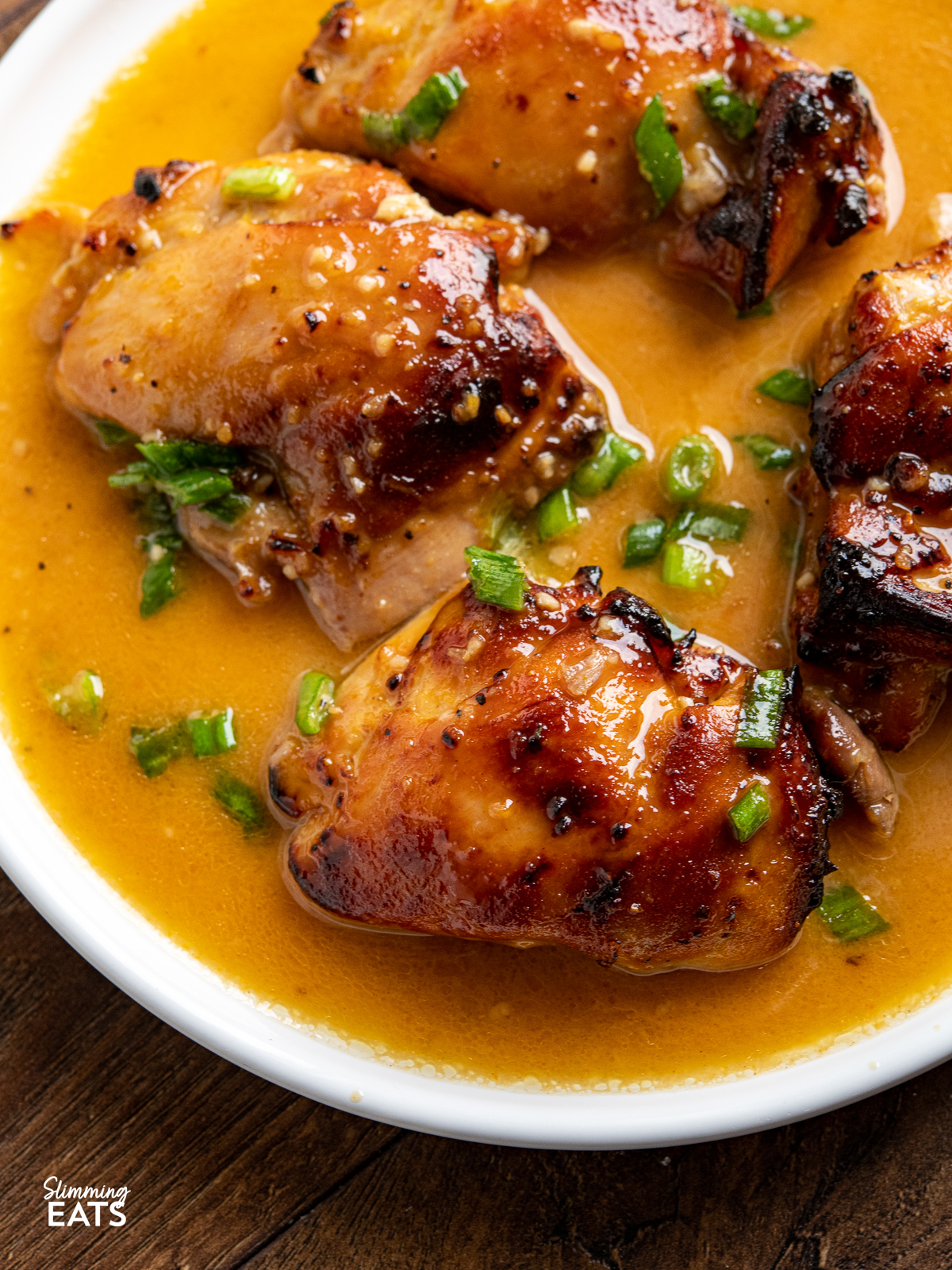 close up of orange dijon chicken thighs on white plate with sauce