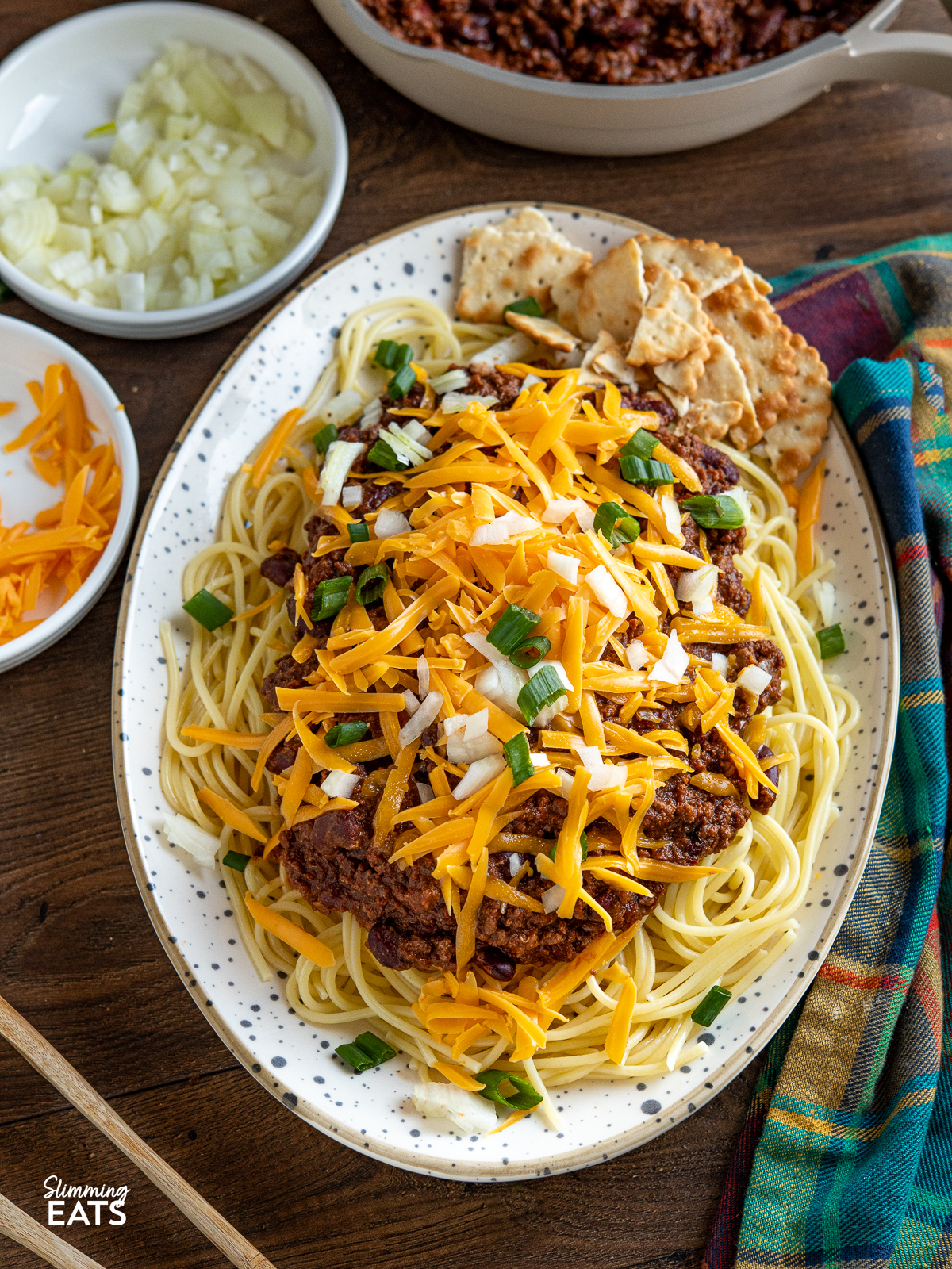 Cincinnati Chili on spotted oval plate with spaghetti and toppings of cheese, onions and salted crackers