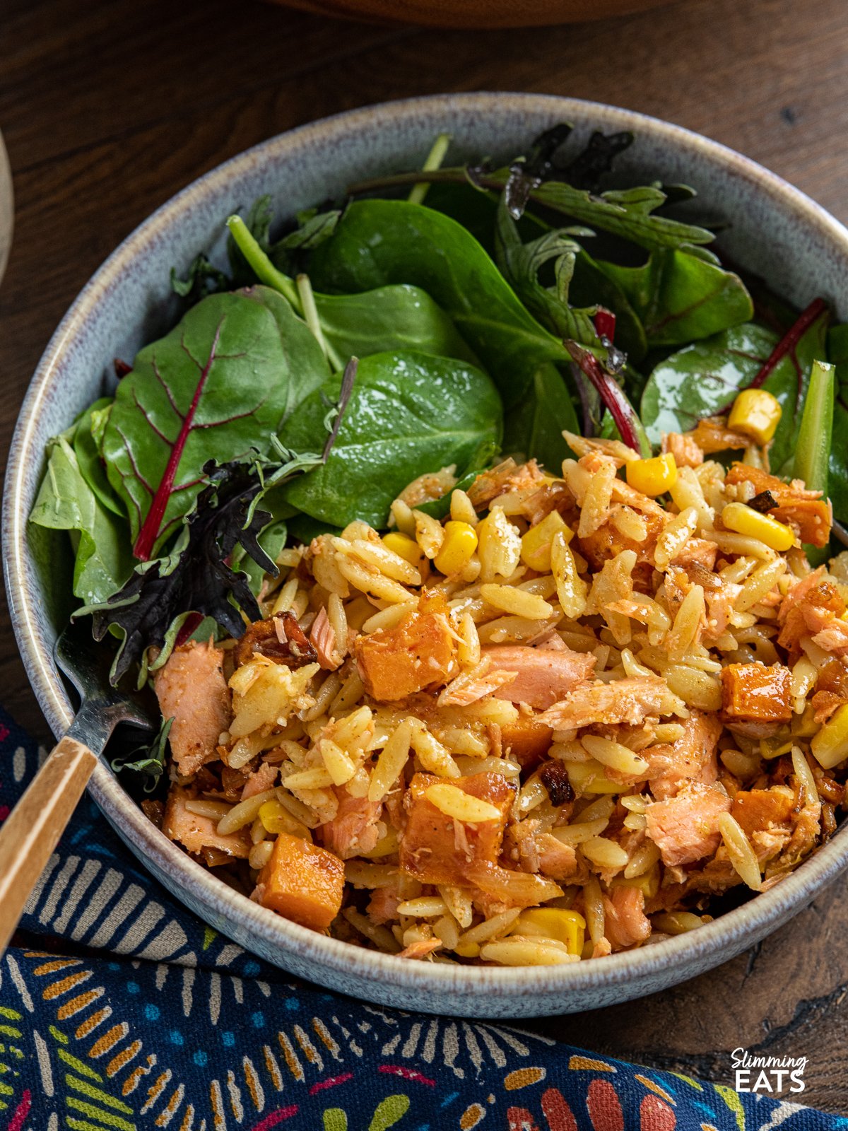 close up of serving of Salmon, Sweet Potato, Corn and Orzo Salad in blue bowl with baby greens 