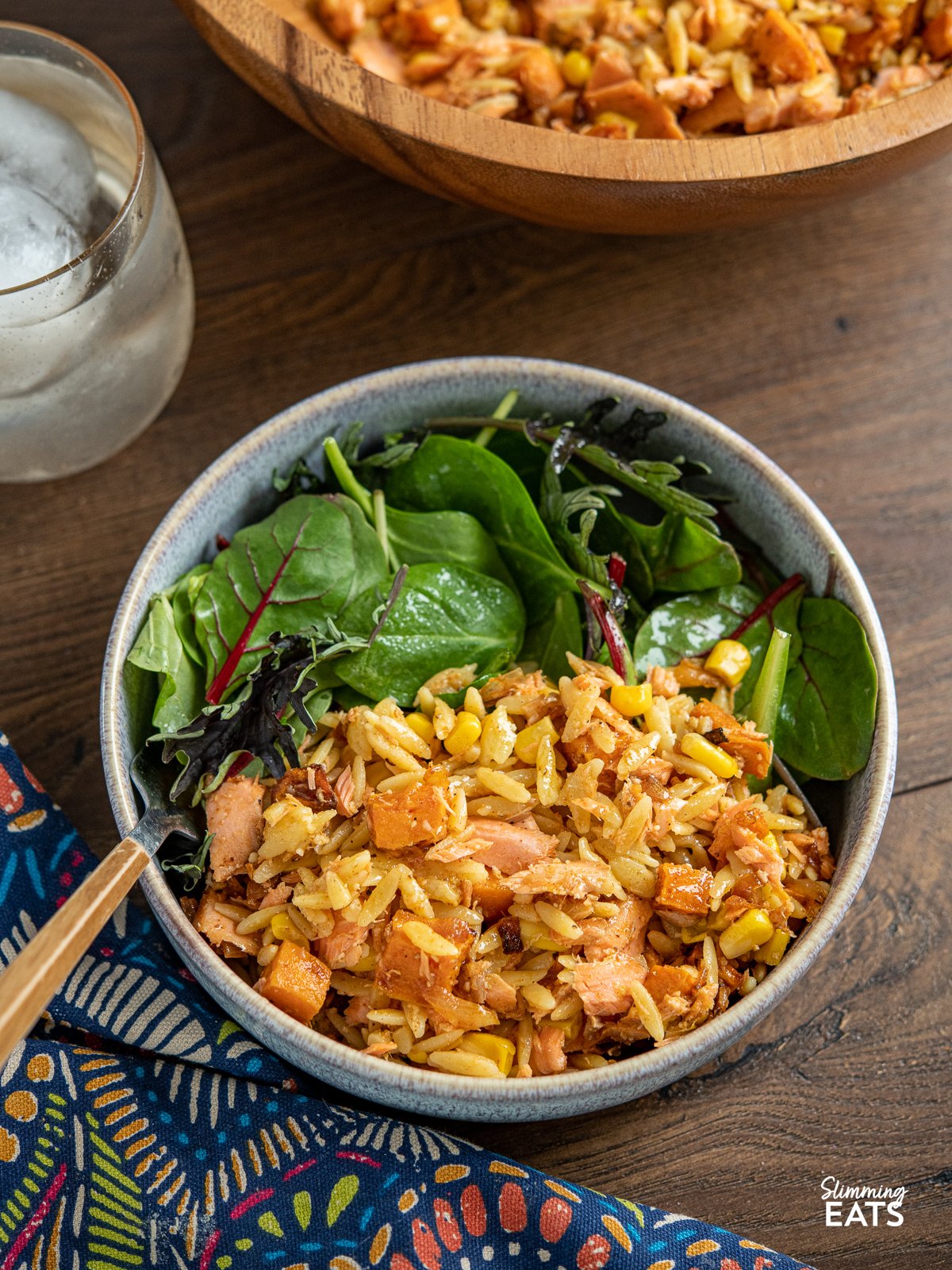 serving of Salmon, Sweet Potato, Corn and Orzo Salad in blue bowl with baby greens