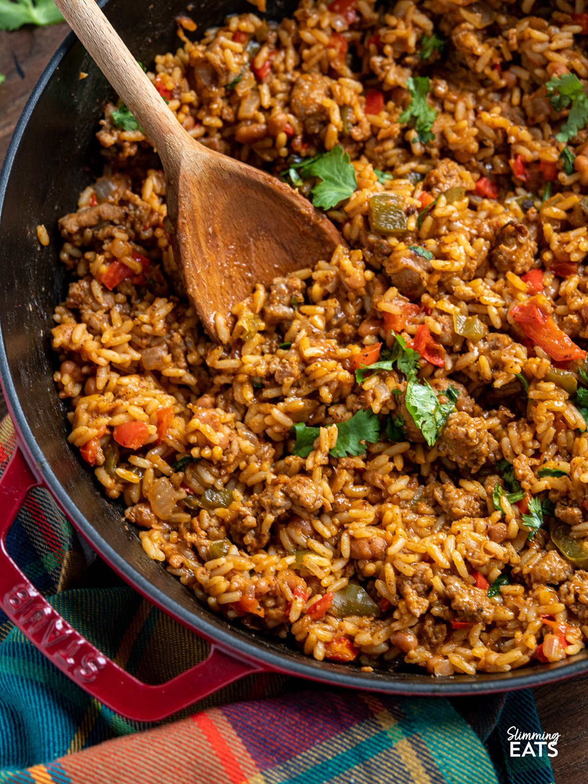 Dig in and enjoy this quick and hearty one-pot meal, packed with sausage, rice, tangy baked beans and BBQ sauce giving it the ultimate smoky campfire flavours. close up One Pot Cowboy Rice in a cherry staub cast iron skillet with wooden spoon