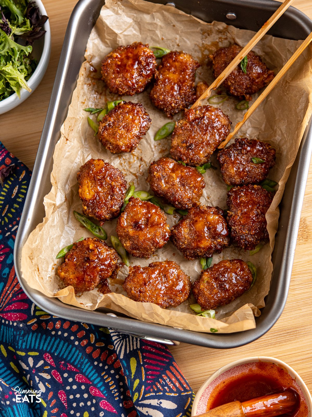 Air Fryer Honey BBQ Chicken Nuggets in metal baking dish with parchment and wooden tongs