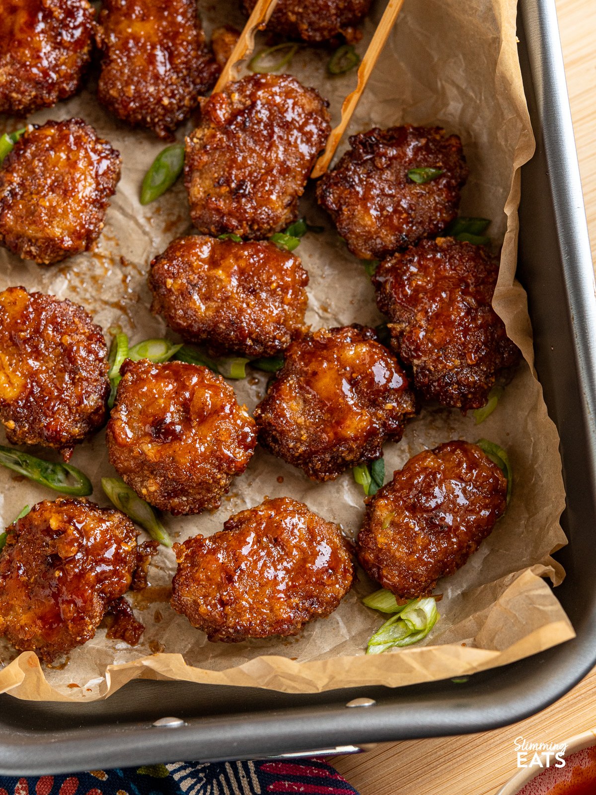 Air Fryer Honey BBQ Chicken Nuggets on a baking tray with parchment paper and wooden tongs