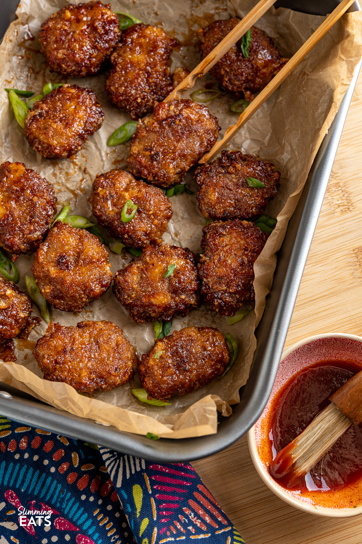 Air Fryer Honey BBQ Chicken Nuggets on a baking tray with parchment paper and wooden tong