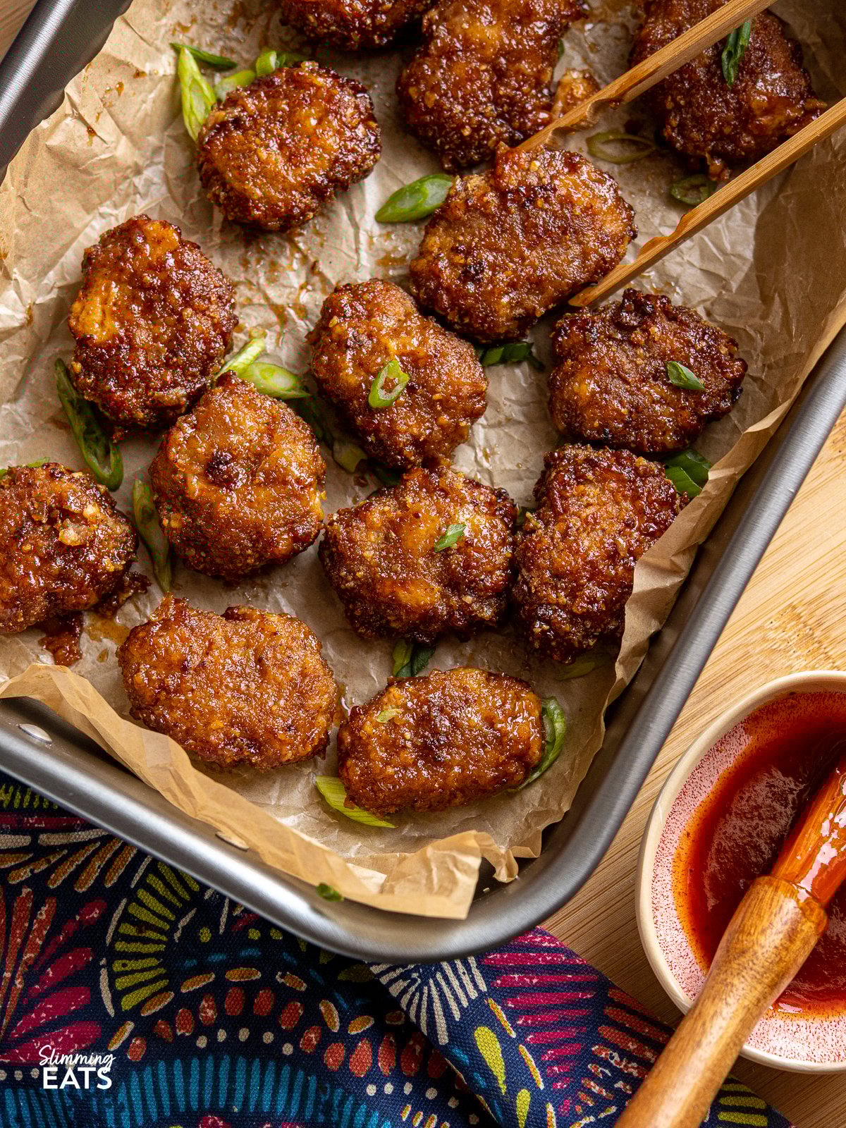 Craving chicken nuggets? Try this homemade honey BBQ chicken cheddar nuggets recipe cooked in an air fryer for a low-calorie, crispy and flavorful treat! Perfect for a quick and easy main meal with some sides or a light bite with a salad. Air Fryer Honey BBQ Chicken Nuggets in a baking tray with parchment and small dish with bbq sauce and brush