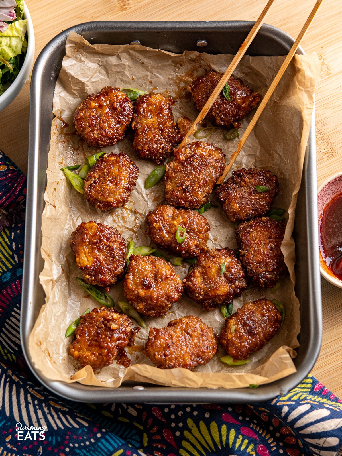 Air Fryer Honey BBQ Chicken Nuggets on a baking tray with parchment paper and wooden tongs