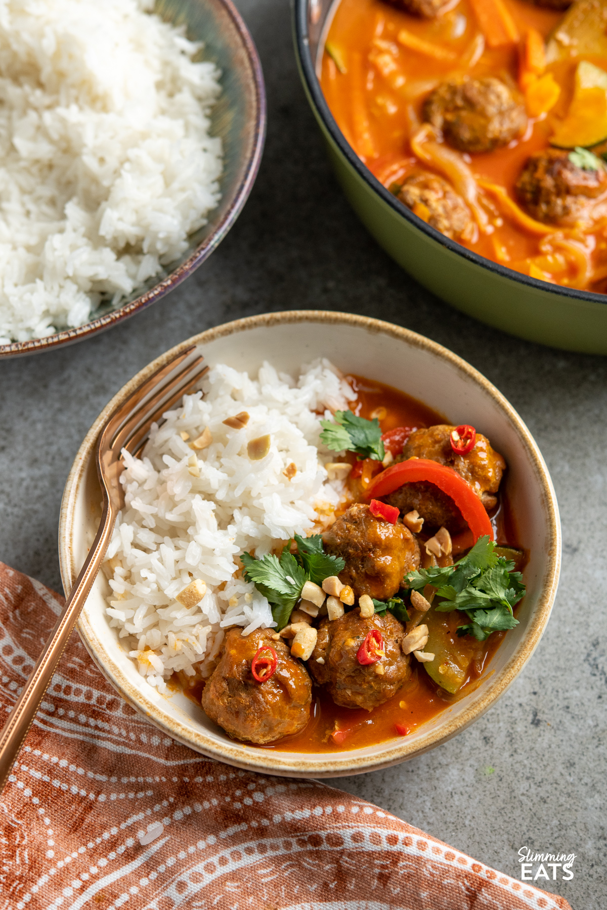 serving of Thai Red Turkey Meatball Curry in bowl with white rice sprinkled with coriander, peanut and red chili 