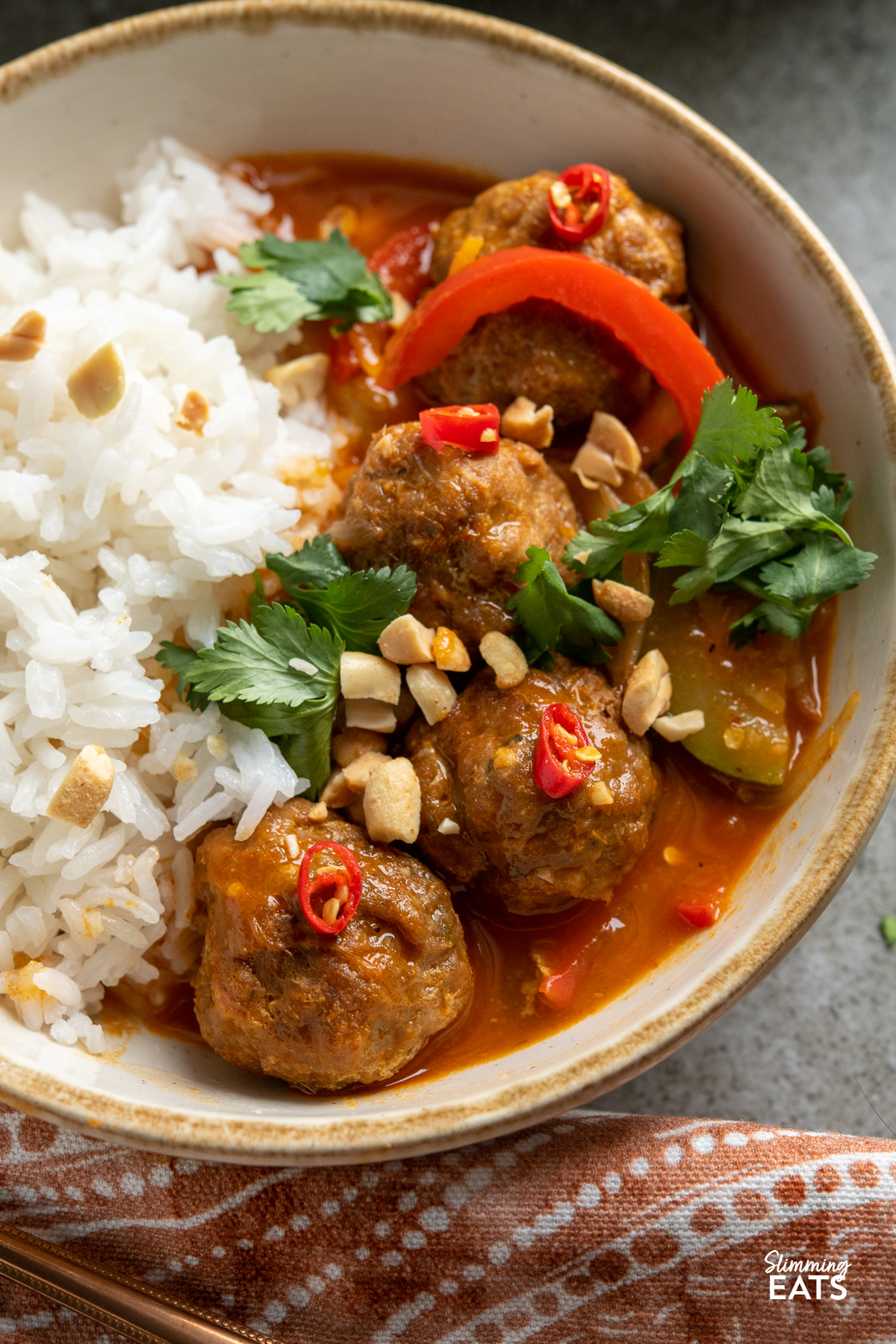 close up serving of Thai Red Turkey Meatball Curry in bowl with white rice sprinkled with coriander, peanut and red chili 