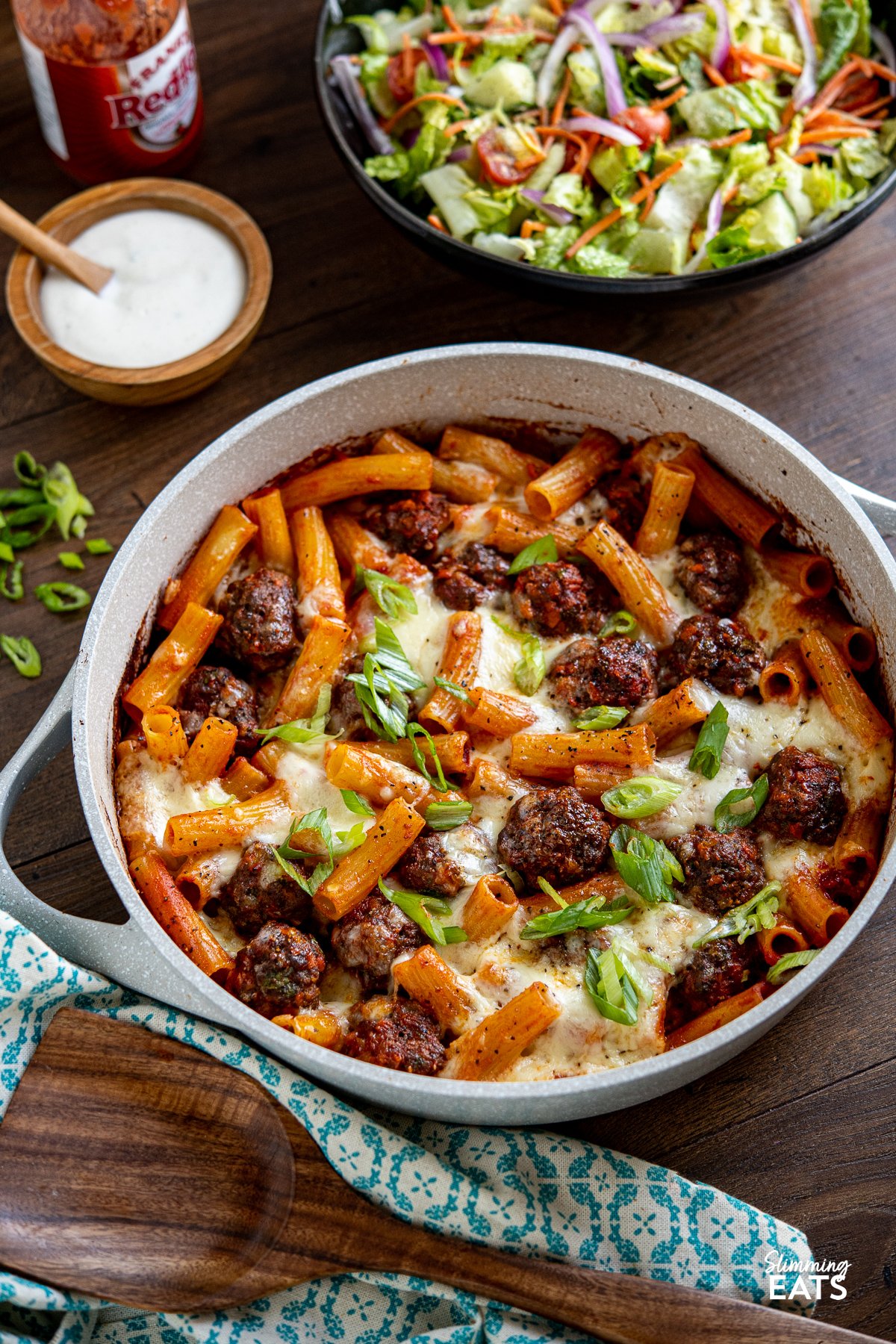 meatballs with pasta and melted mozzarella topping in ceramic coated pan with side salad in black bowl