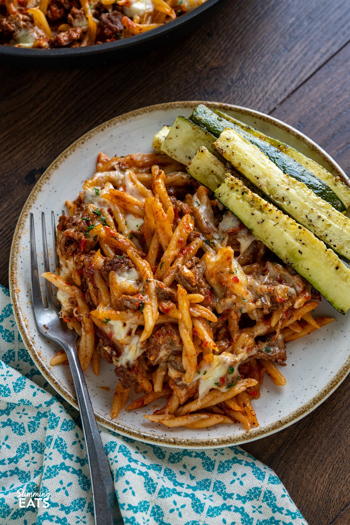 serving of Creamy Beef Roasted Red Pepper Pasta Bake with roasted zucchini on a white plate with beige rim fork placed to the left