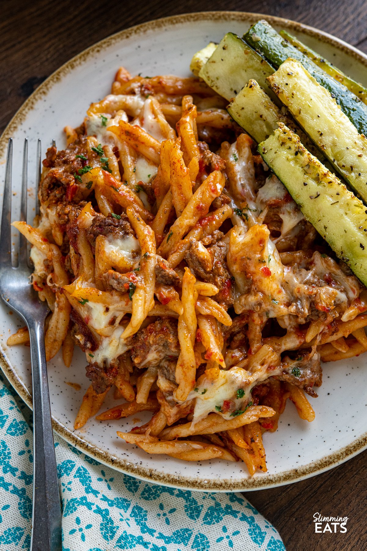 close up of serving of Creamy Beef Roasted Red Pepper Pasta Bake with roasted zucchini on a white plate with beige rim fork placed to the left