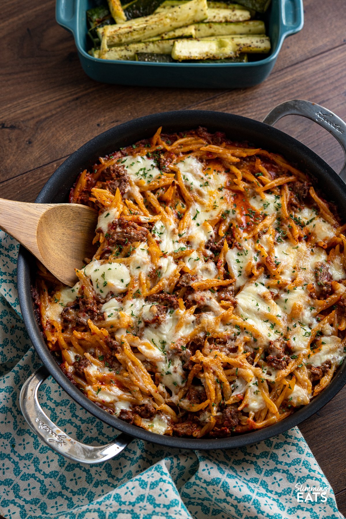 Creamy Beef Roasted Red Pepper Pasta Bake - Indulge in the ultimate comfort food with our creamy ground beef pasta recipe. This delectable dish features trofie pasta, roasted red peppers, and a heavenly blend of torn mozzarella and Parmesan. Baked to perfection, each bite is a symphony of flavors that will leave you craving more. Get ready to experience a mouthwatering culinary delight like no other. Creamy Beef Roasted Red Pepper Pasta Bake in double handled black frying pan with oven dish with roasted zucchini