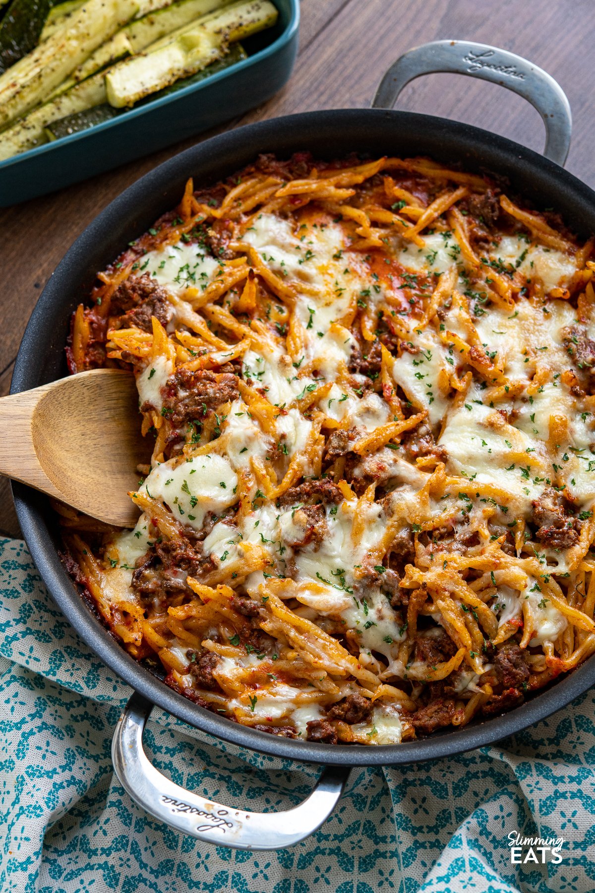 Creamy Beef Roasted Red Pepper Pasta Bake - Indulge in the ultimate comfort food with our creamy ground beef pasta recipe. This delectable dish features trofie pasta, roasted red peppers, and a heavenly blend of torn mozzarella and Parmesan. Baked to perfection, each bite is a symphony of flavors that will leave you craving more. Get ready to experience a mouthwatering culinary delight like no other. Creamy Beef Roasted Red Pepper Pasta Bake in double handled black frying pan with oven dish with roasted zucchini