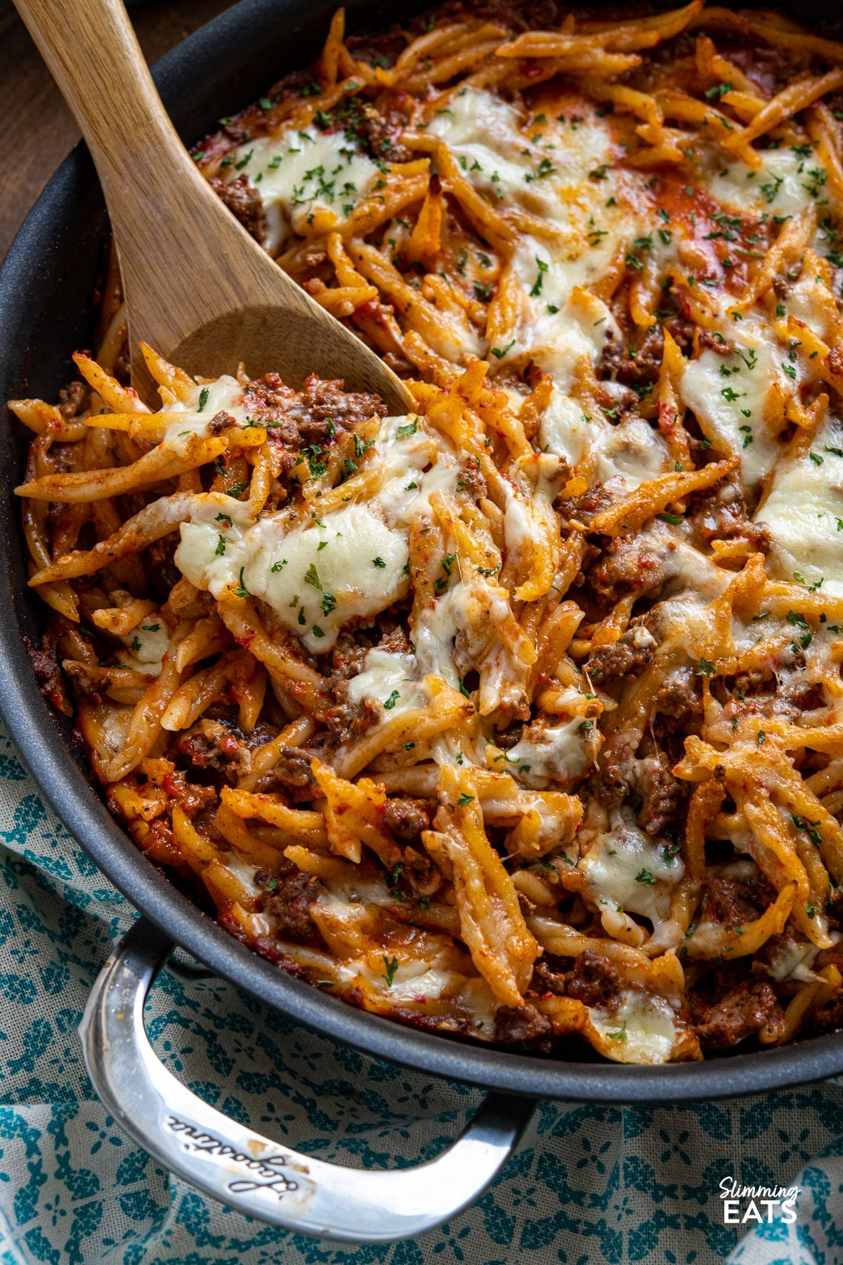 Creamy Beef Roasted Red Pepper Pasta Bake - Indulge in the ultimate comfort food with our creamy ground beef pasta recipe. This delectable dish features trofie pasta, roasted red peppers, and a heavenly blend of torn mozzarella and Parmesan. Baked to perfection, each bite is a symphony of flavors that will leave you craving more. Get ready to experience a mouthwatering culinary delight like no other. close up of Creamy Beef Roasted Red Pepper Pasta Bake in double handled black frying pan