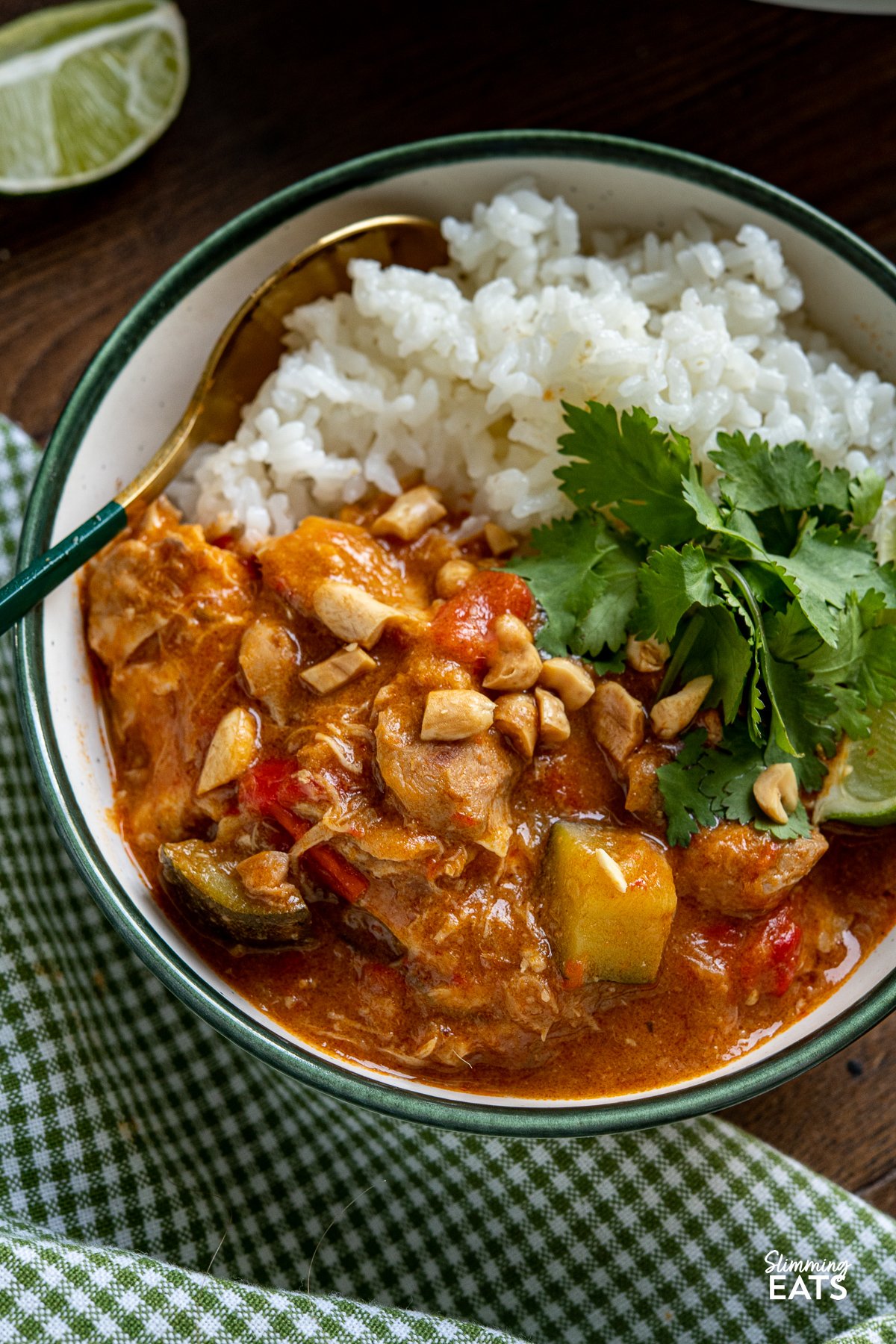 close up of serving of Slow Cooker Thai Peanut Chicken Curry with white rice and chopped peanuts, coriander and lime wedge