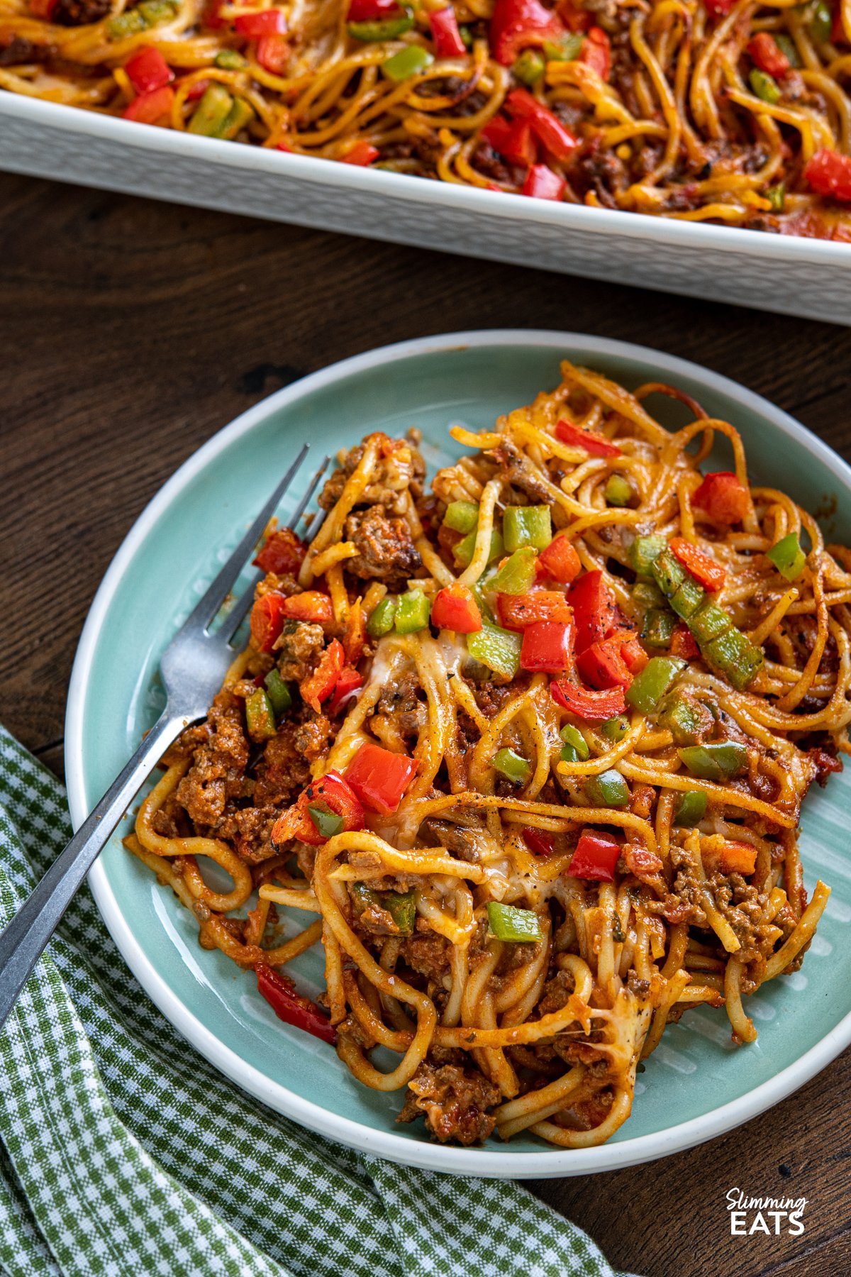 serving of taco spaghetti bake in white oven proof dish on turquoise and white plate with fork to left