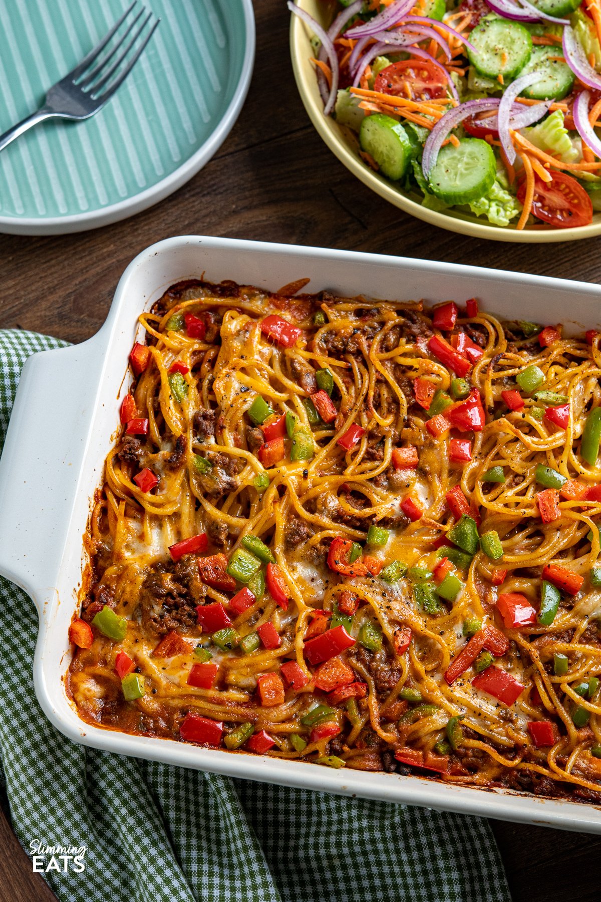 Baked Cheesy Taco SpaghettI - flavourful taco meat sauce, tangy salsa, and al dente spaghetti baked together to perfection, topped with a generous layer of gooey melted cheese and colorful bell peppers. It's a delightful blend of Tex-Mex flavors that will instantly become a family favourite. taco spaghetti bake in white oven proof dish