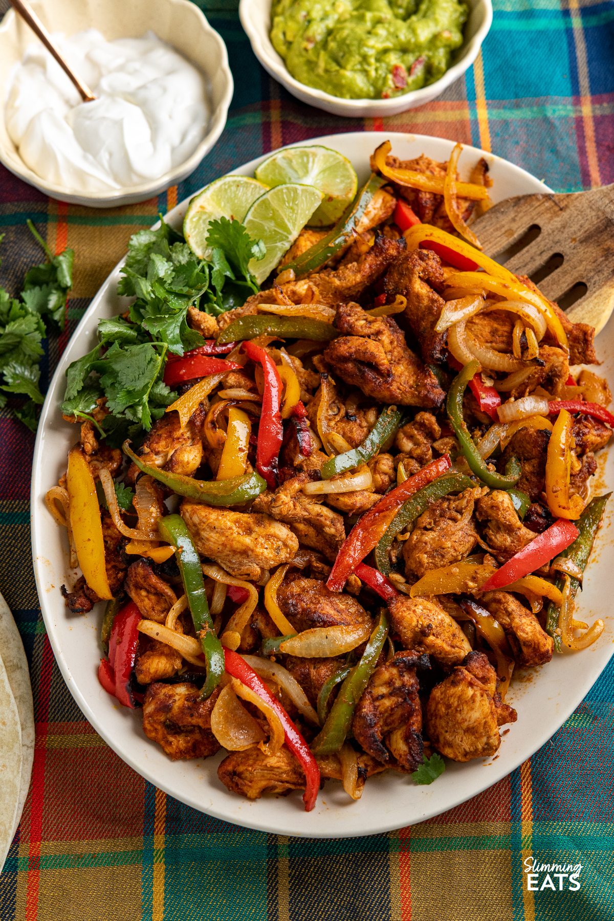 Air Fryer Chicken Fajitas on a large oval plate with small bowls of guacamole and soured cream to the side.