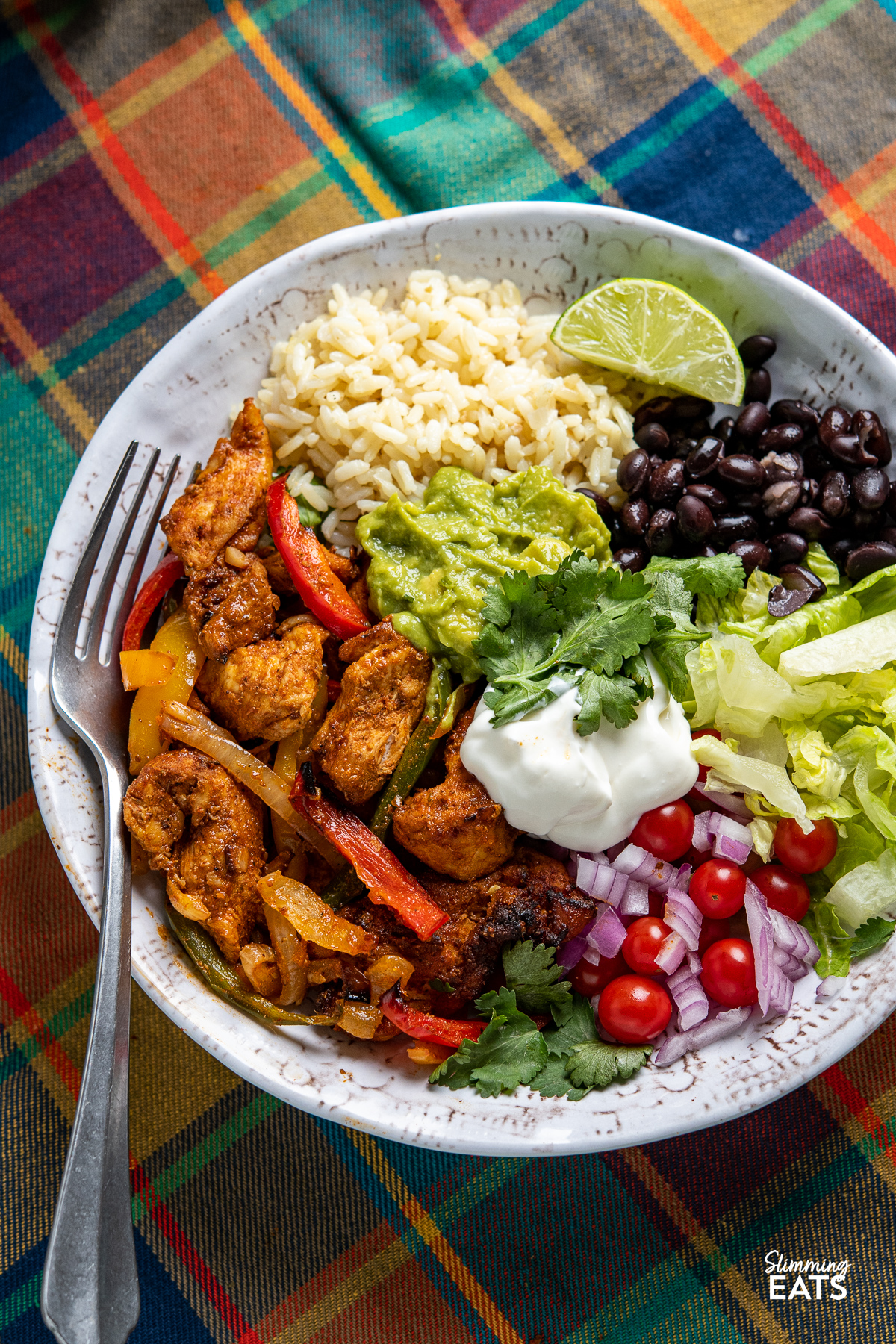 Chicken Fajita bowl with rice, lettuce, black beans, soured cream, guacamole, red onion and tomatoes.