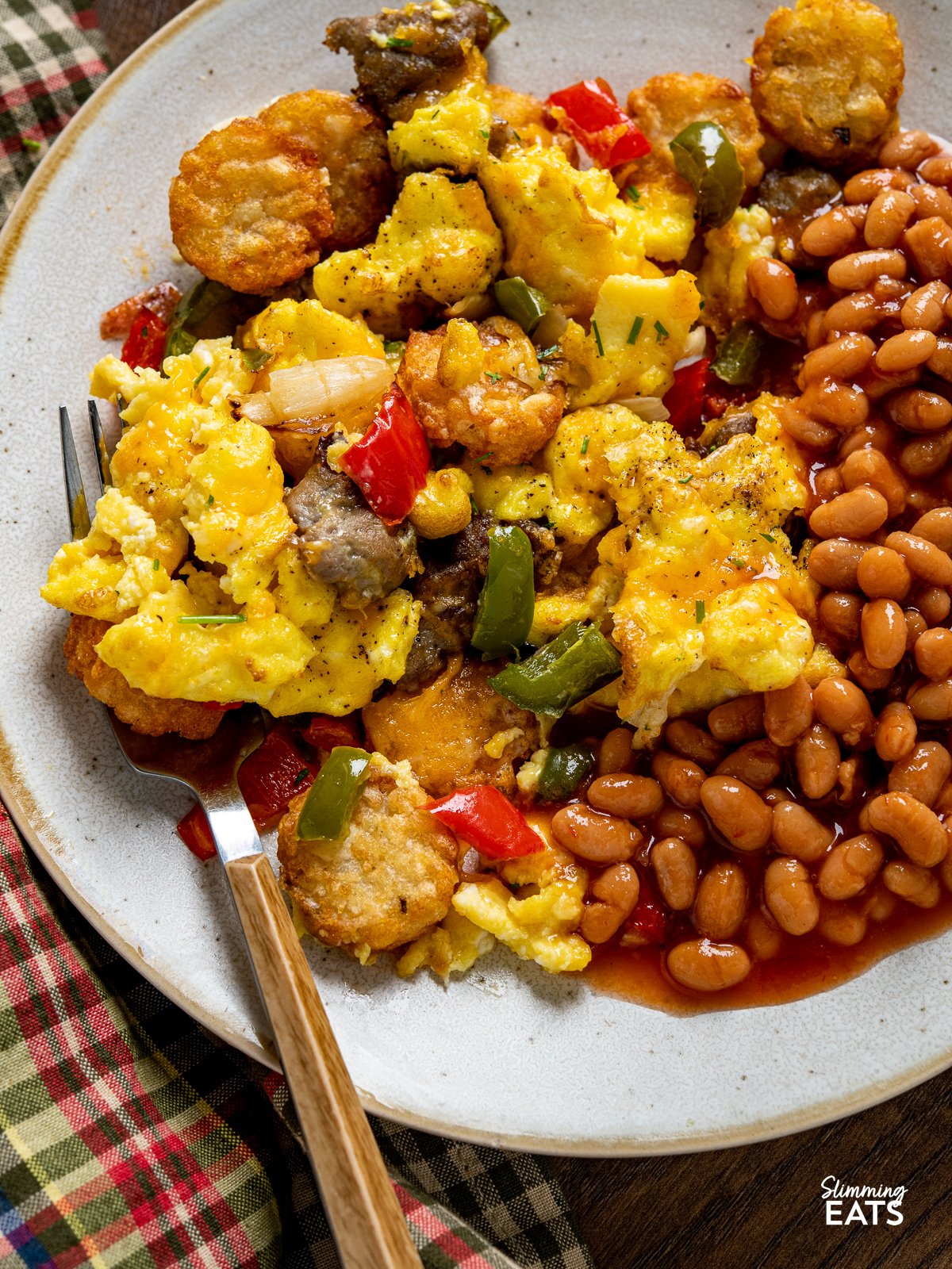 Indulge in the savoury delight of golden and crunchy Crispy Air Fried Tater Tots (Hash Brown Bites) Totchos, with a blend of sausage, peppers, and sweet onions. Topped with creamy scrambled eggs and a luxurious cascade of melted cheese. close up of Air Fryer Breakfast Loaded Tater Tots (Totchos) on a plate with baked beans
