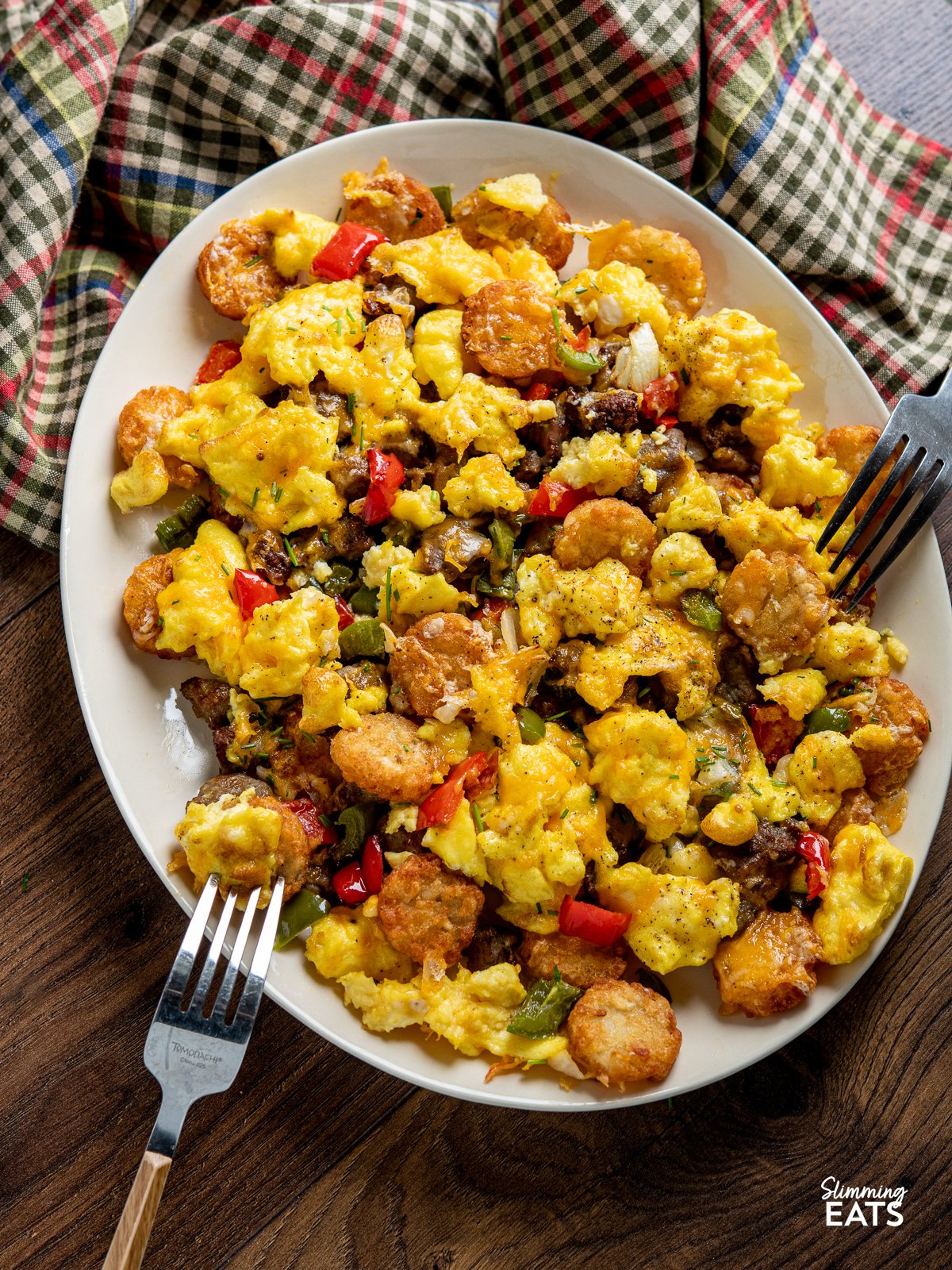Indulge in the savoury delight of golden and crunchy Crispy Air Fried Tater Tots (Hash Brown Bites) Totchos, with a blend of sausage, peppers, and sweet onions. Topped with creamy scrambled eggs and a luxurious cascade of melted cheese. Air Fryer Breakfast Loaded Tater Tots (Totchos) on a oval plate with two forks
