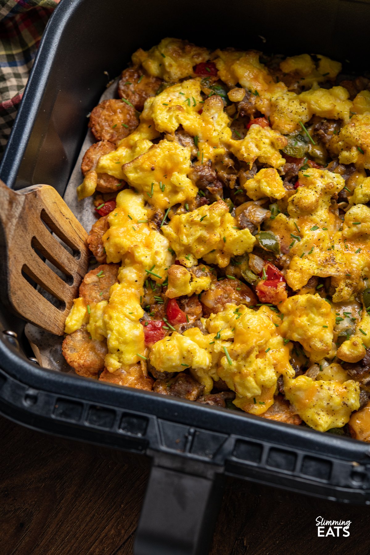 Indulge in the savoury delight of golden and crunchy Crispy Air Fried Tater Tots (Hash Brown Bites) Totchos, with a blend of sausage, peppers, and sweet onions. Topped with creamy scrambled eggs and a luxurious cascade of melted cheese. Air Fryer Breakfast Loaded Tater Tots (Totchos) in an air fryer basket