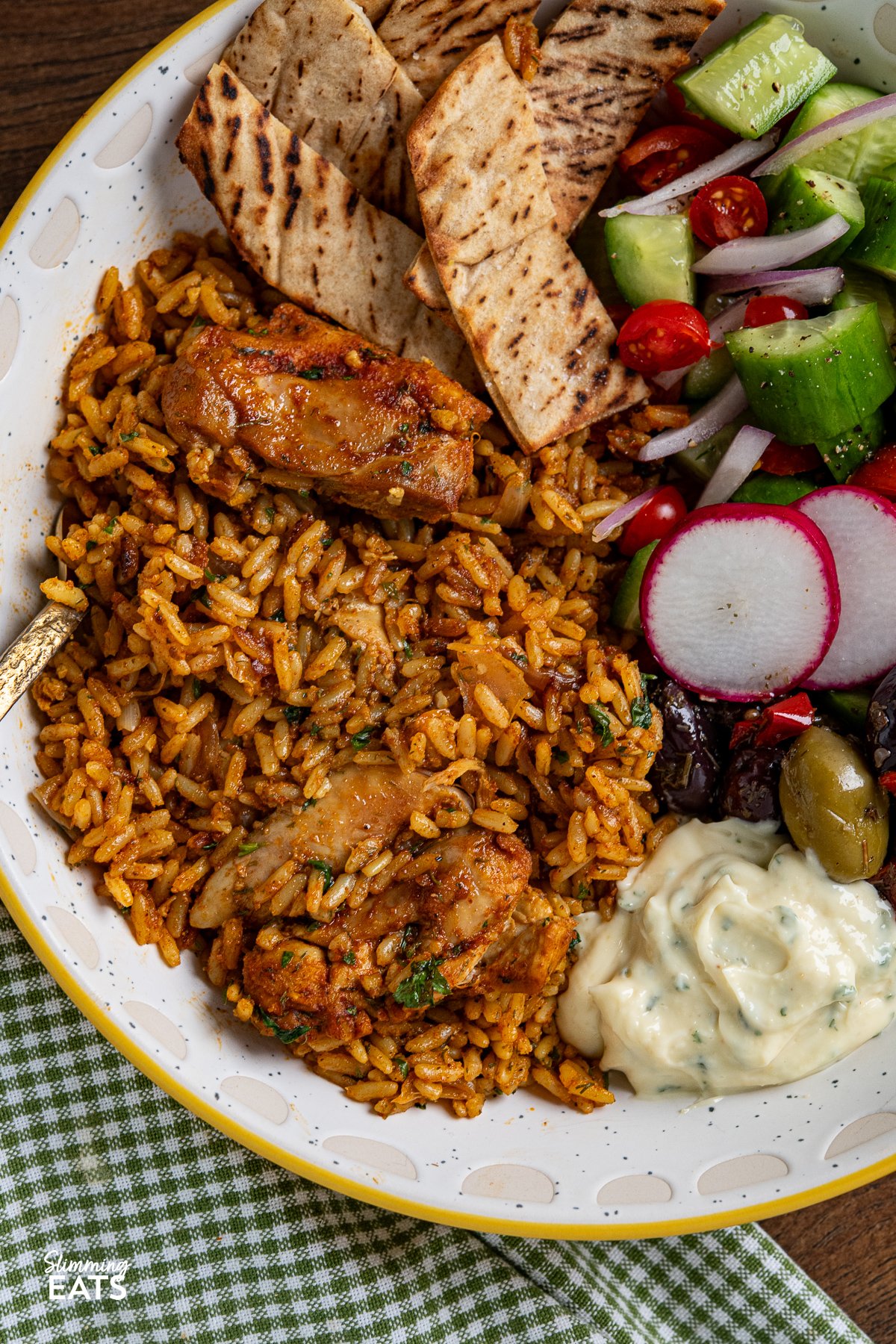 close up of chicken shawarma and rice bowl with olives, cucumber, tomato, red onion and pita bread with garlic sauce