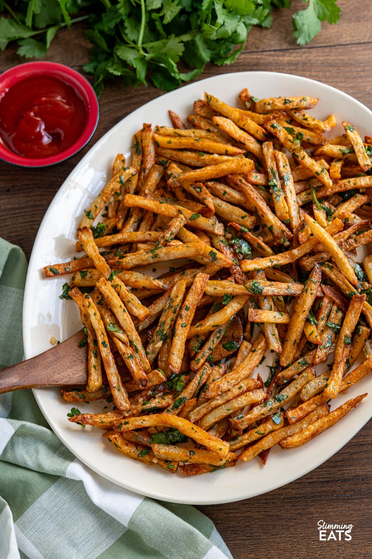 Garlic Cilantro Oven Baked Fries on oval plate with wooden spatula and small red bowl of ketchup