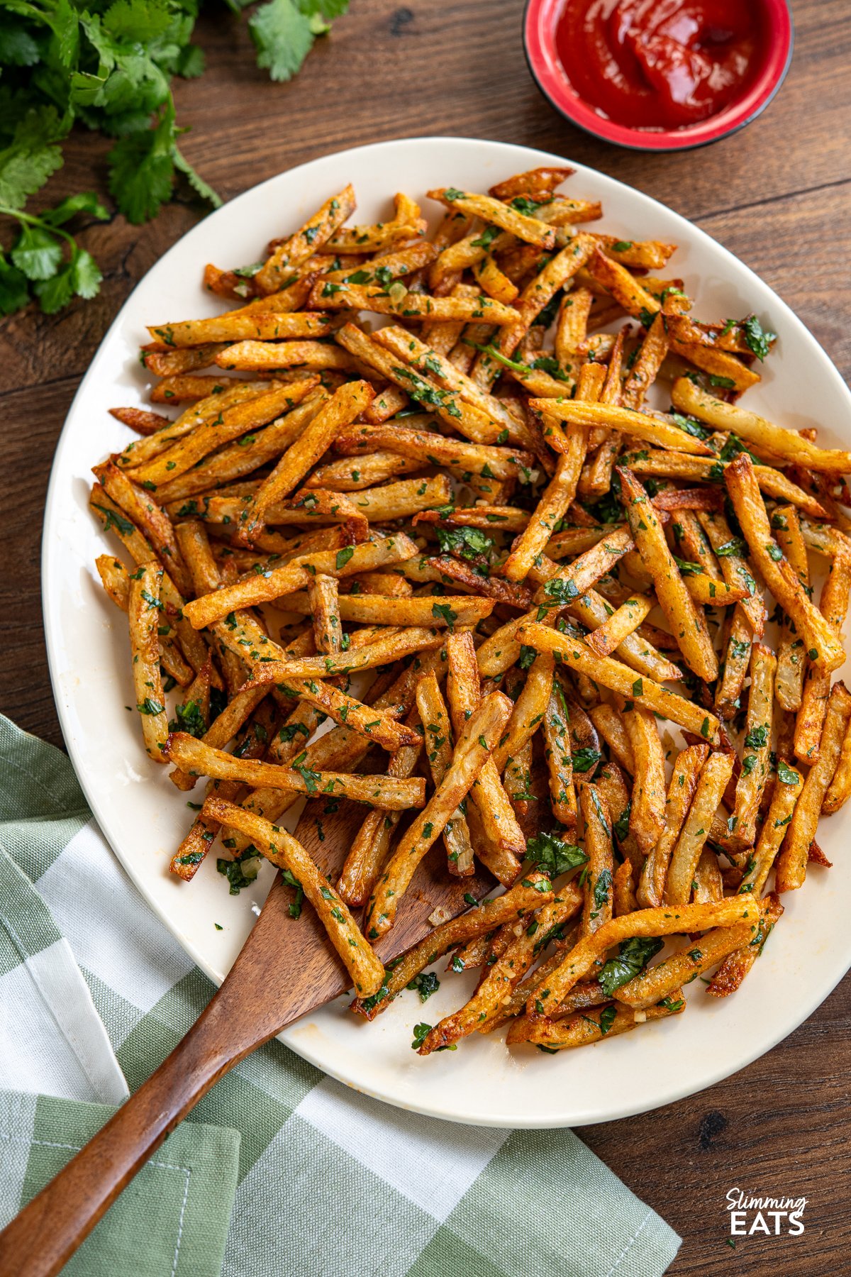 Garlic Cilantro Oven Baked Fries on oval plate with wooden spatula and ketchup in small red bowl